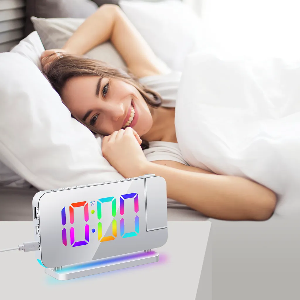 Eine Frau liegt im Bett und lächelt. Ein digitaler Wecker mit Farbdisplay steht daneben.