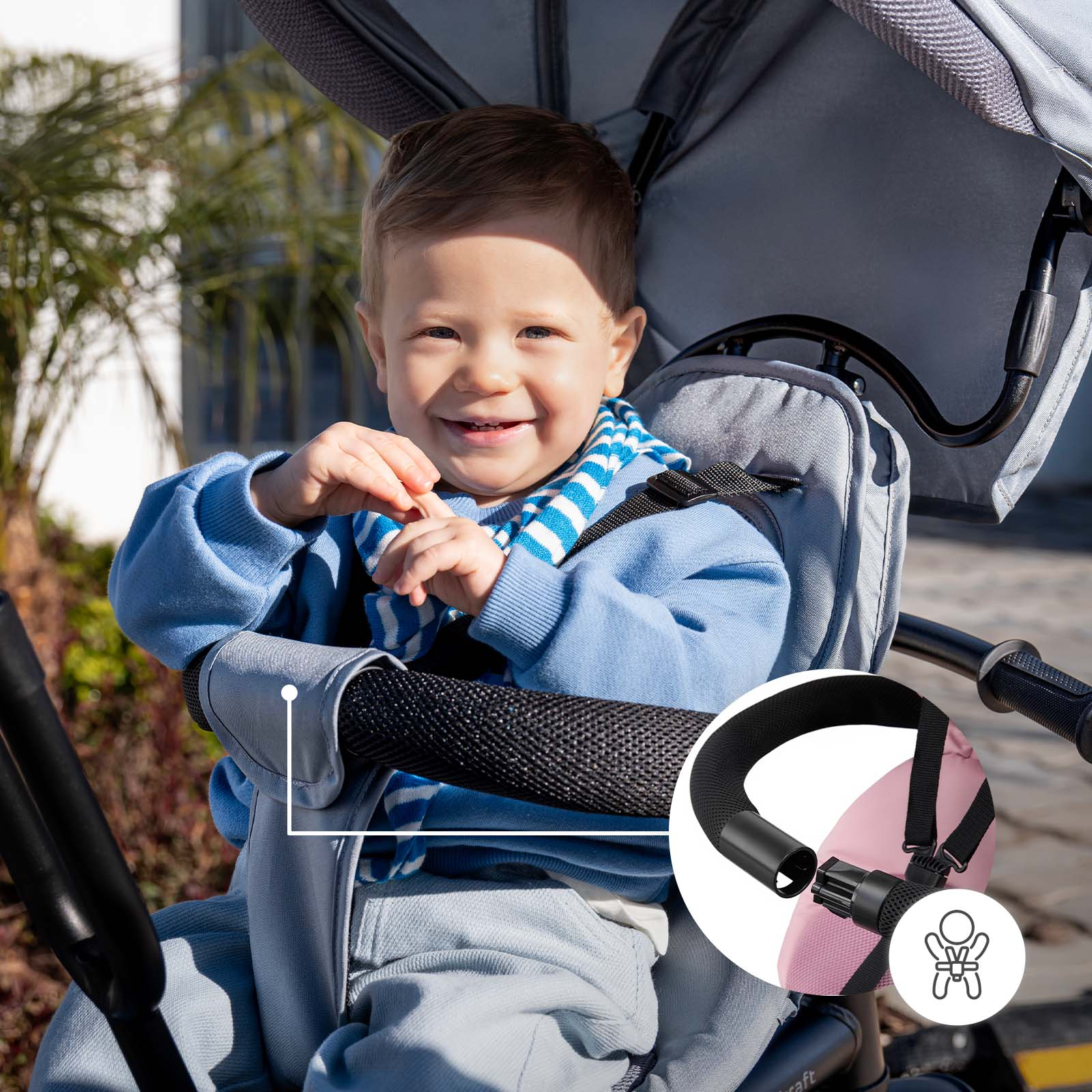 Ein lächelndes Baby sitzt in einem Kinderwagen mit blauem Pullover und Schal.