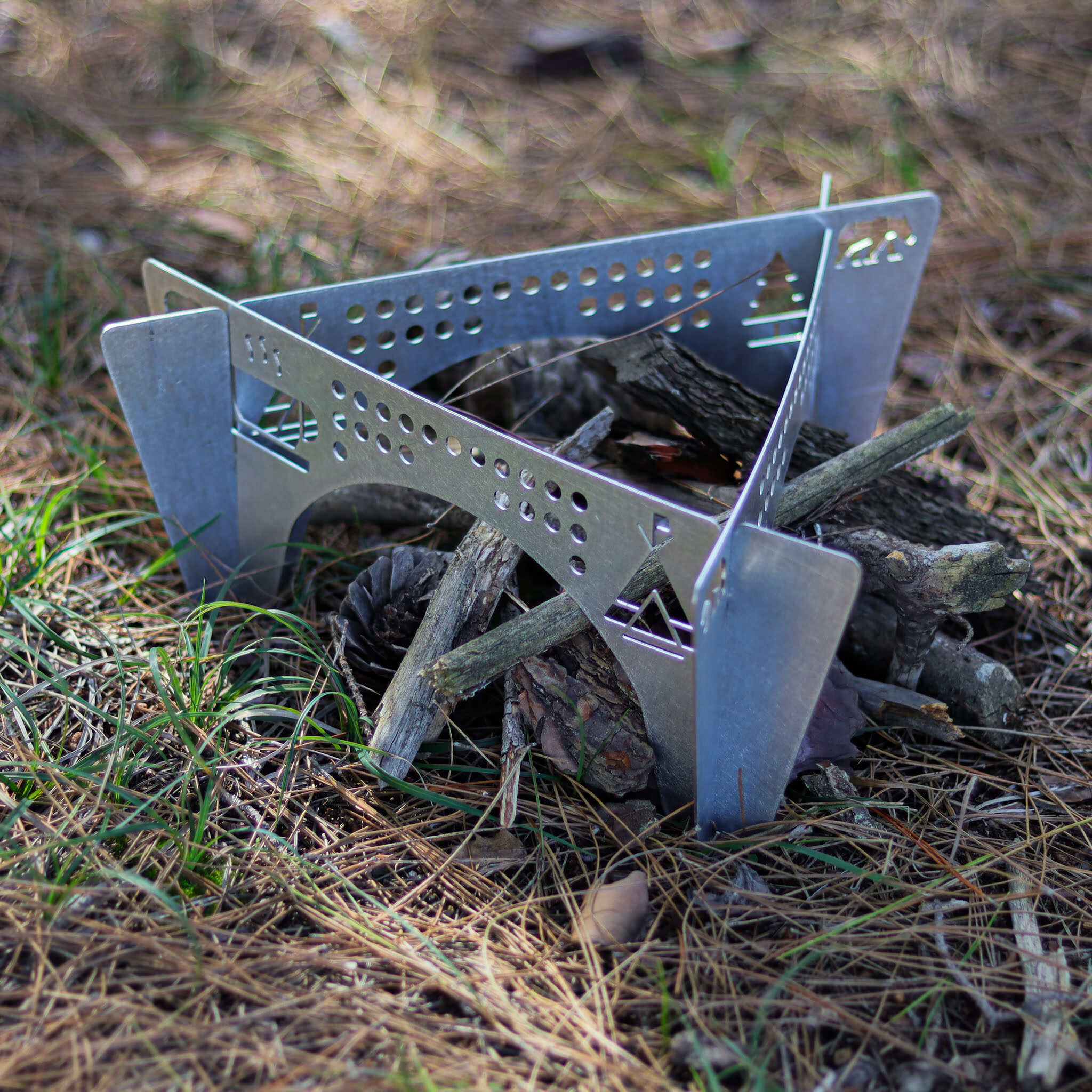 Metal taşınabilir kamp ateşi ızgarası, yerde odun ve kozalaklar.