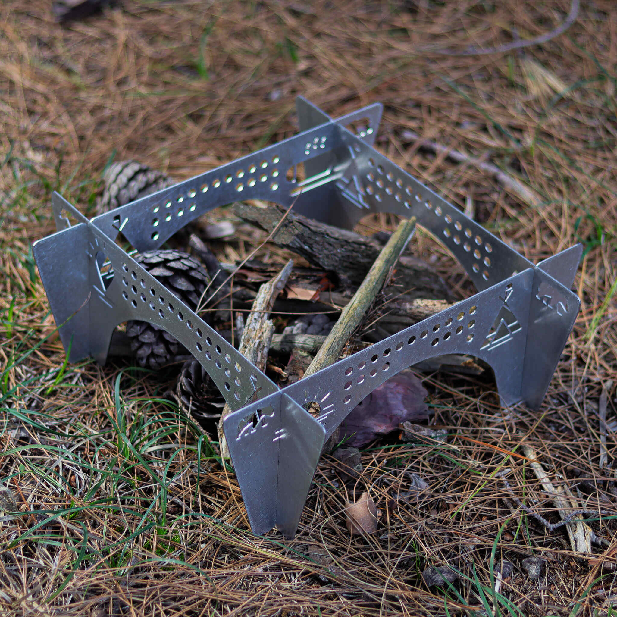 Metal kamp ocağı, çam iğneleri, dallar ve kozalaklar üzerinde.