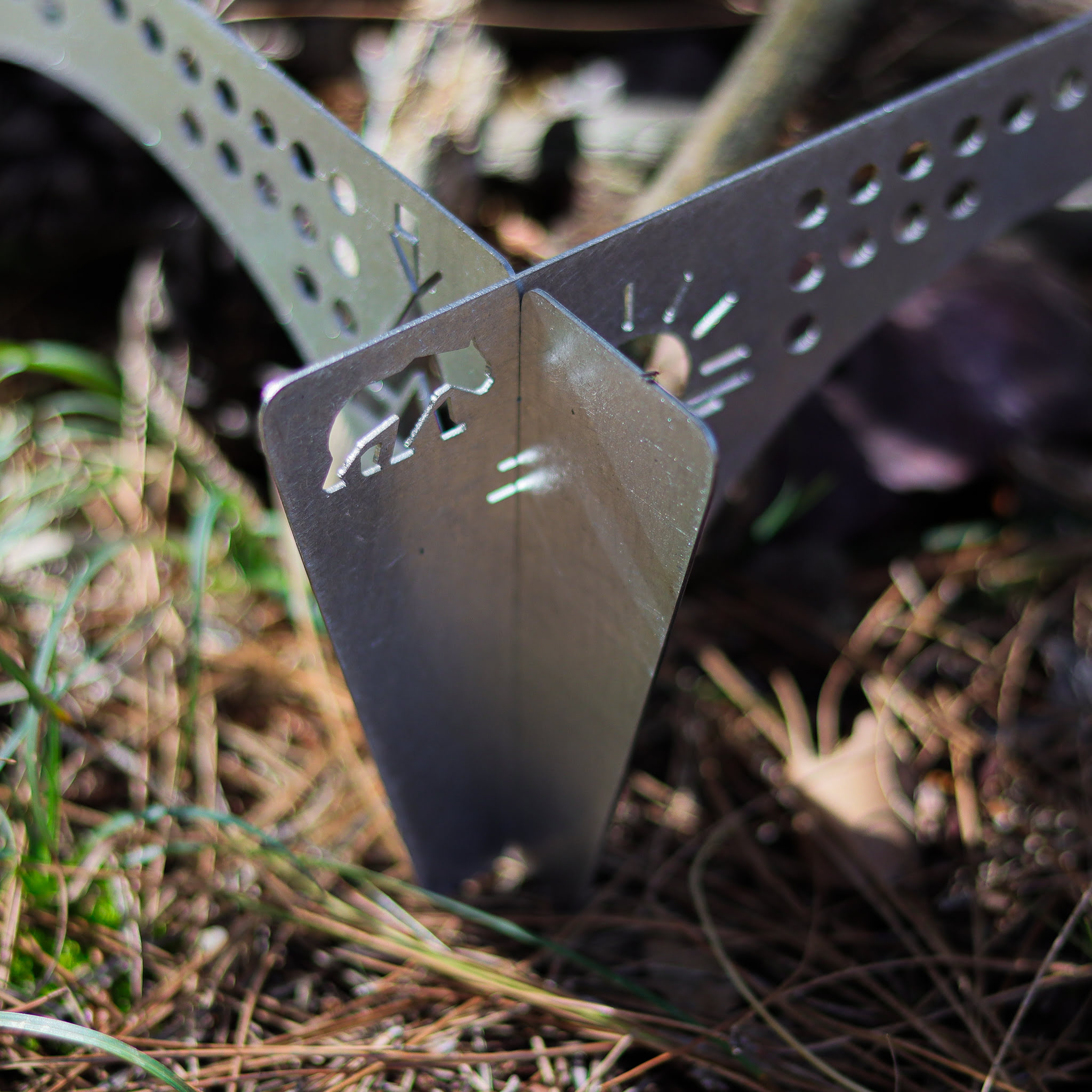 Gümüş metal obje, üzerinde ayı silüeti kesiği, kuru yaprakların üzerinde.