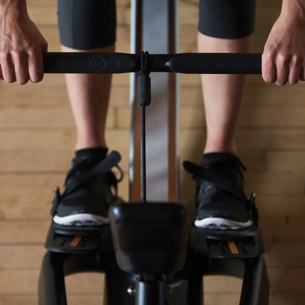 Person rowing, holding handle, wearing black shoes and black shorts.