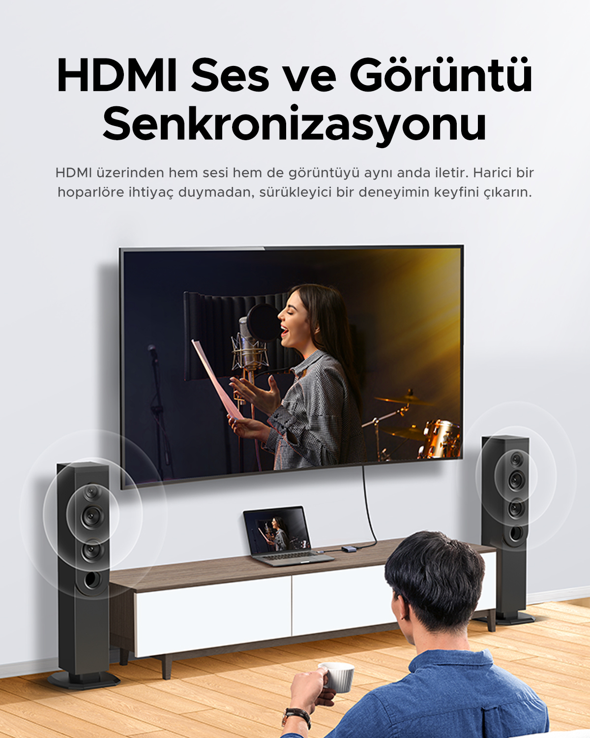 Bir adam şarkıcıyı gösteren TV'yi izliyor. Sol ve sağda hoparlörler var.