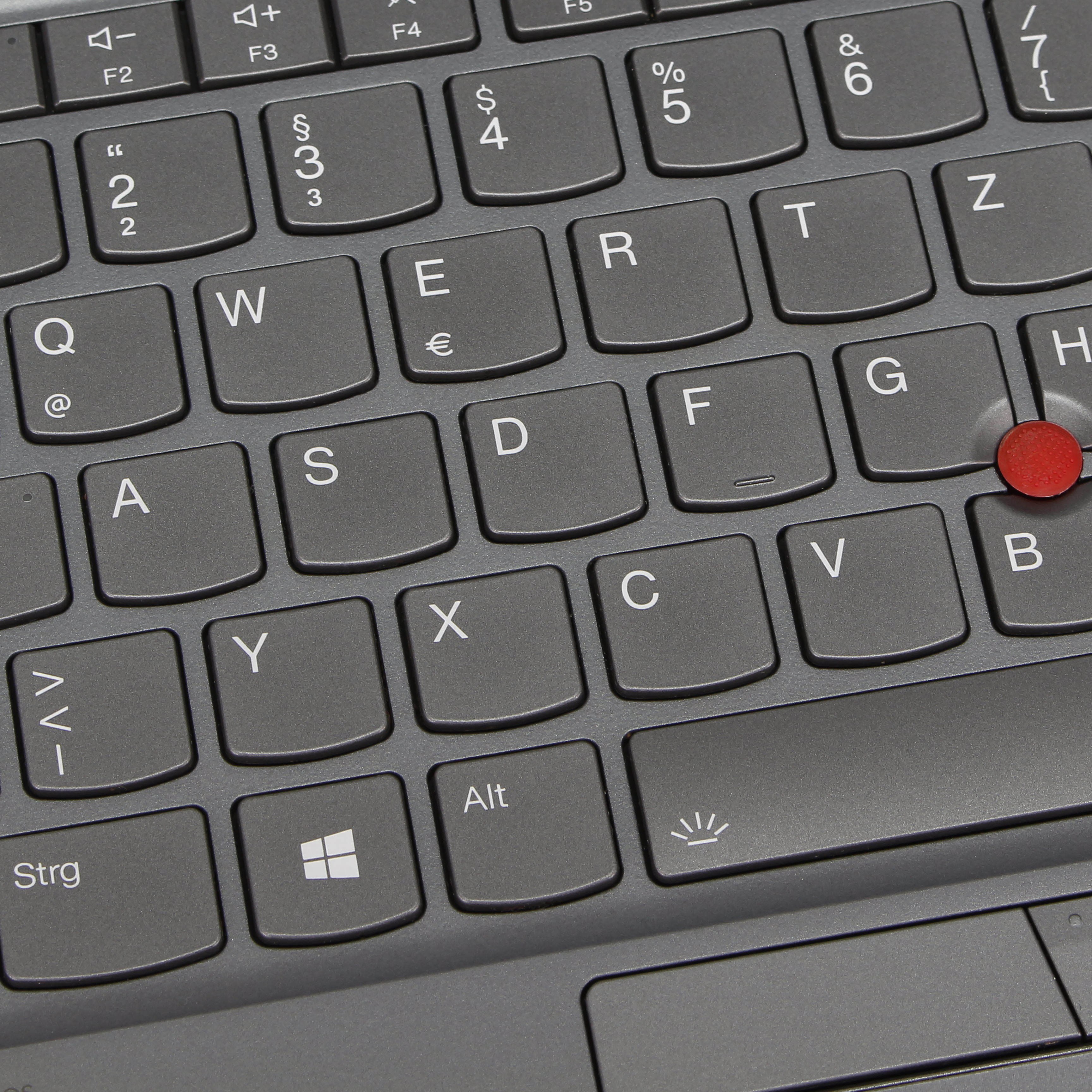 Primo piano di una tastiera grigio scuro con lettere, numeri e simboli. È visibile un trackpoint rosso.