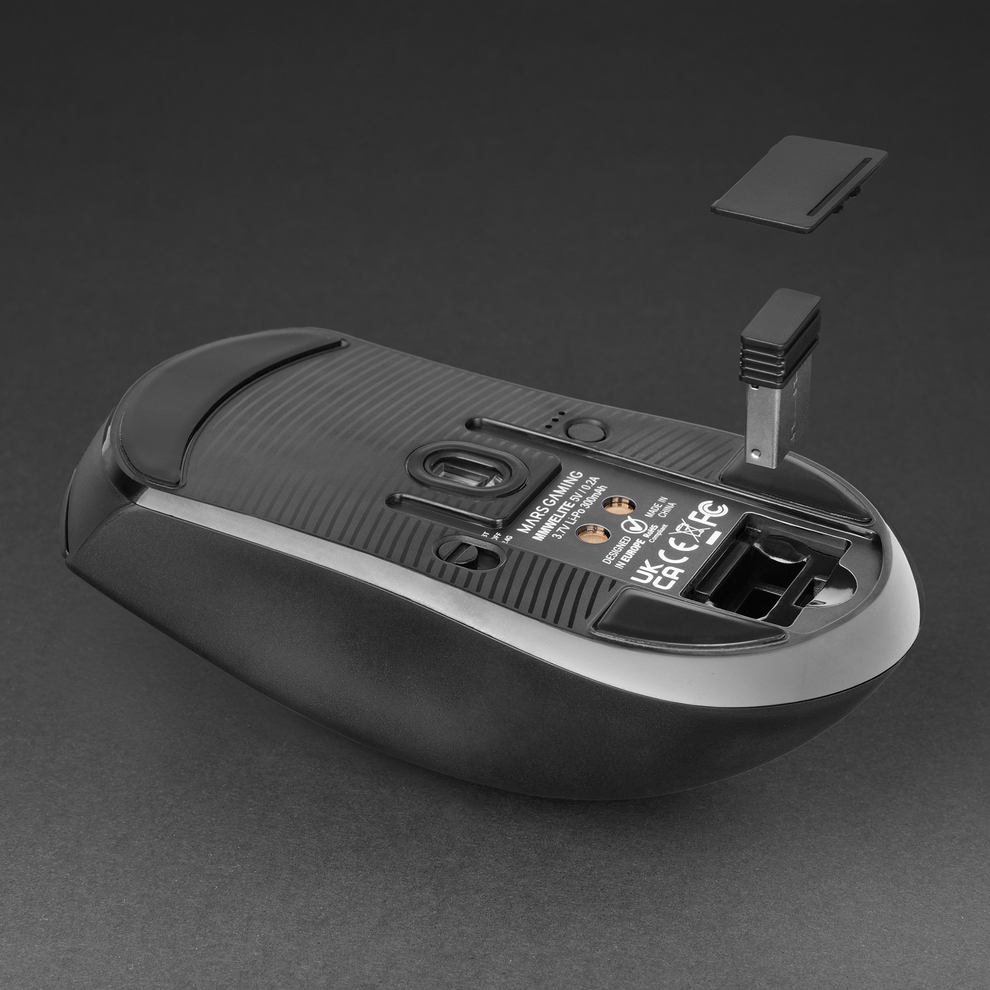 Parte inferiore di un mouse nero con dongle USB e coperchio rimossi.