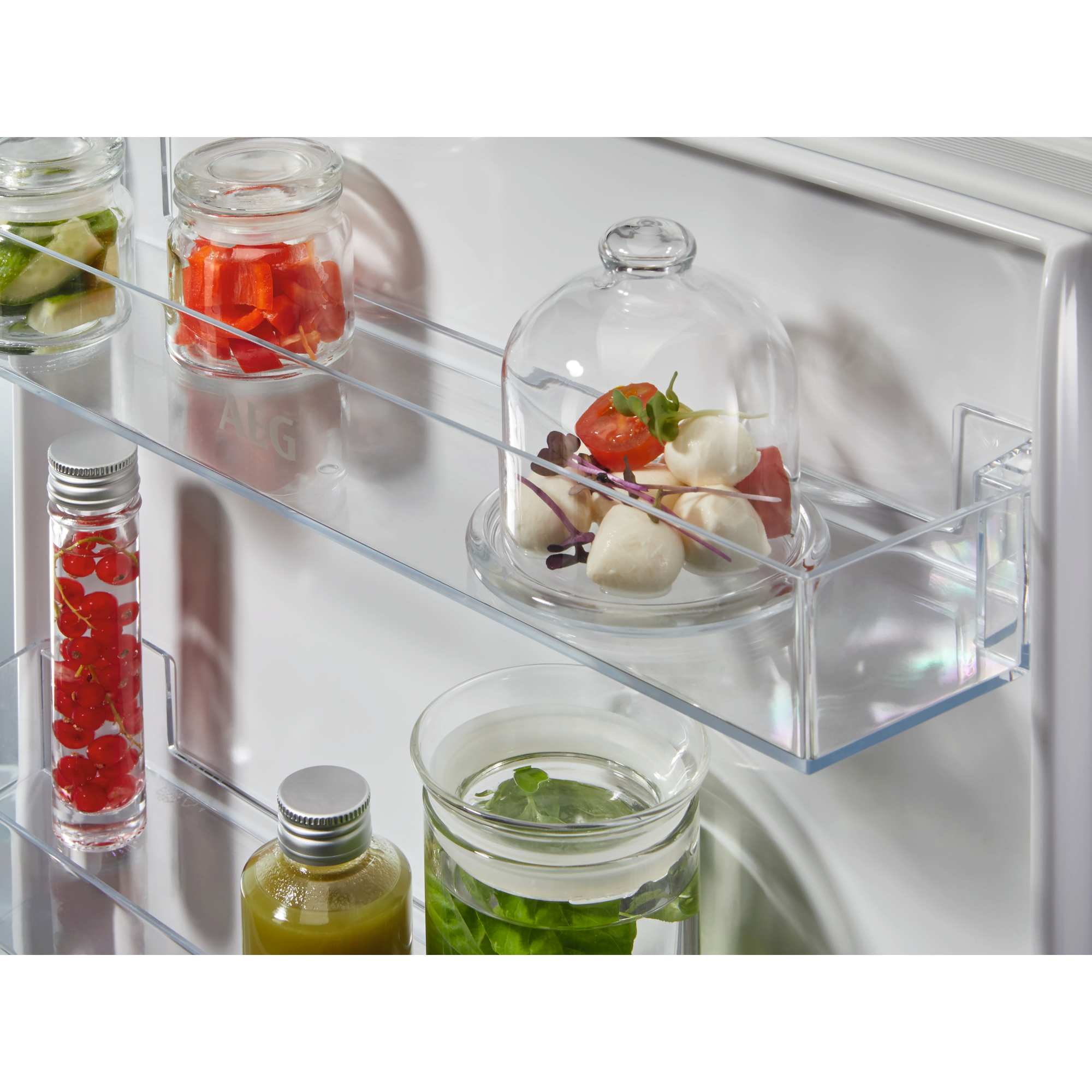 Varios alimentos en recipientes de vidrio en estantes de refrigerador.