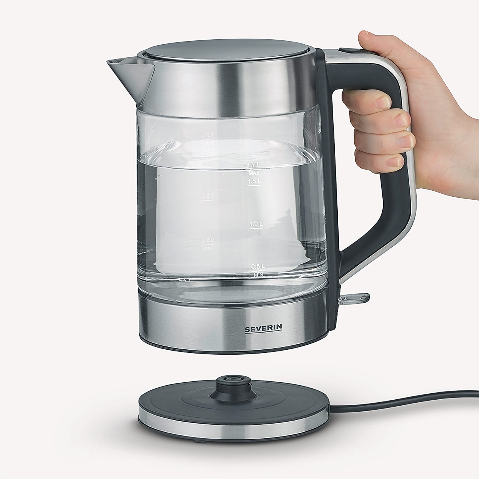 Een hand houdt een glazen waterkoker met water boven de basis vast.