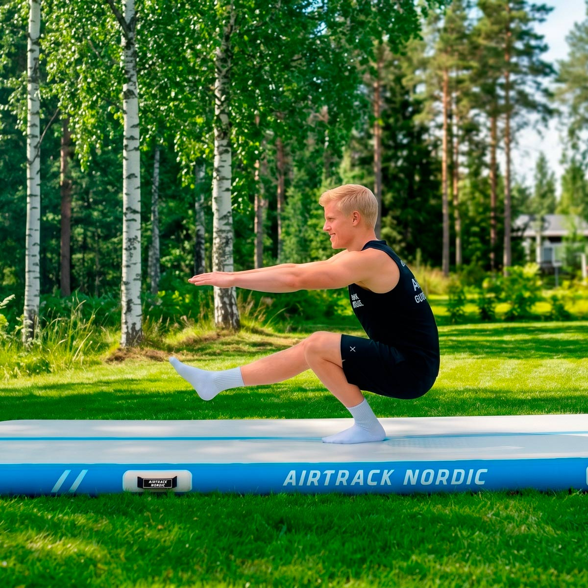 Mann macht einen Pistol Squat auf einer Airtrack im Gras mit Bäumen.