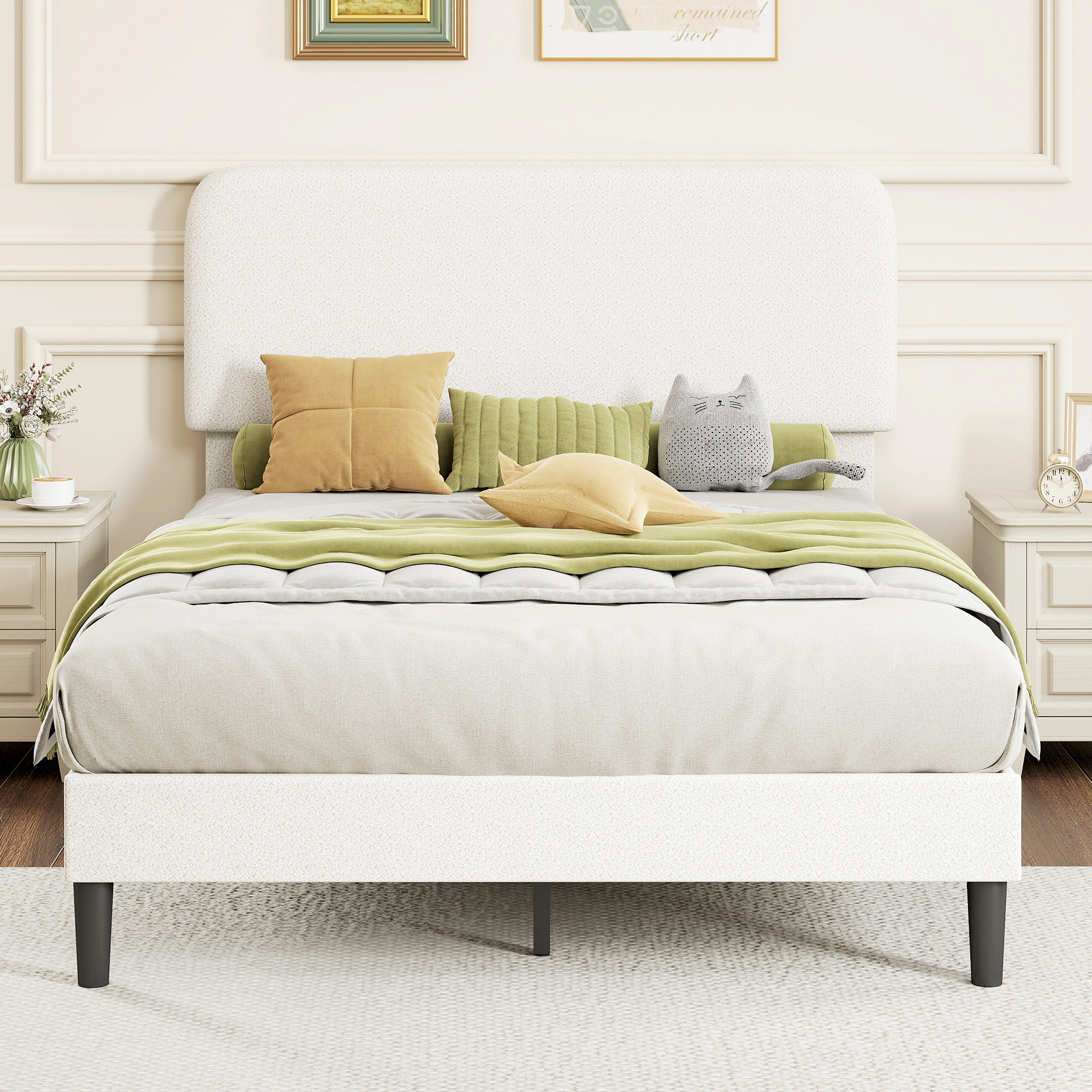 Una cama tapizada blanca con almohadas amarillas y verdes y una almohada de gato.