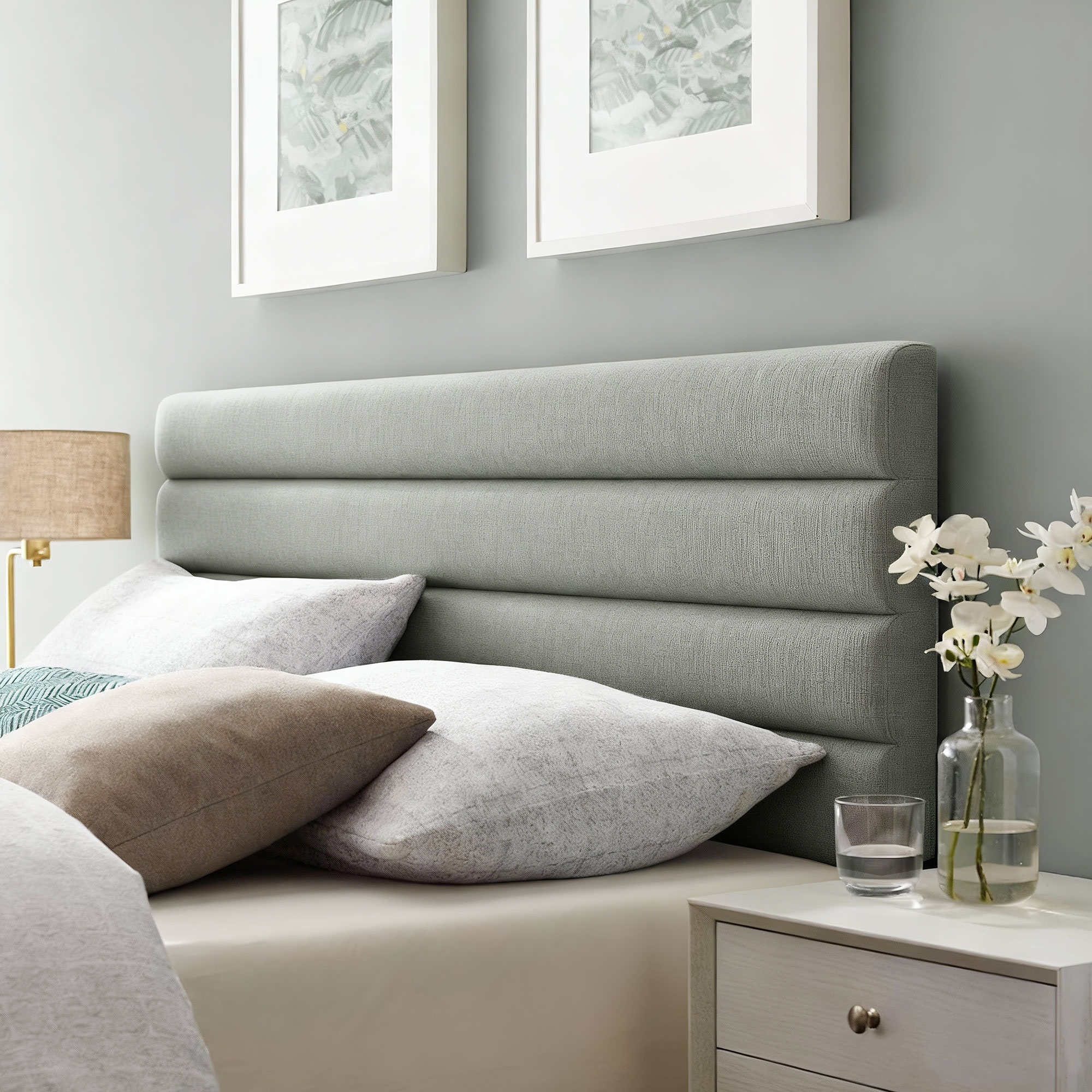 Un cabecero gris acolchado sobre una cama con cojines y un jarrón con orquídeas.