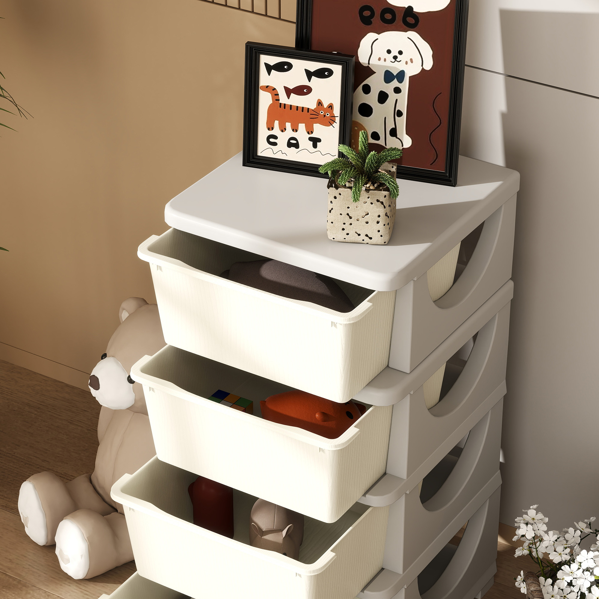 Una unidad de almacenamiento blanca con cajones, llena de juguetes y ropa, junto a un osito de peluche.