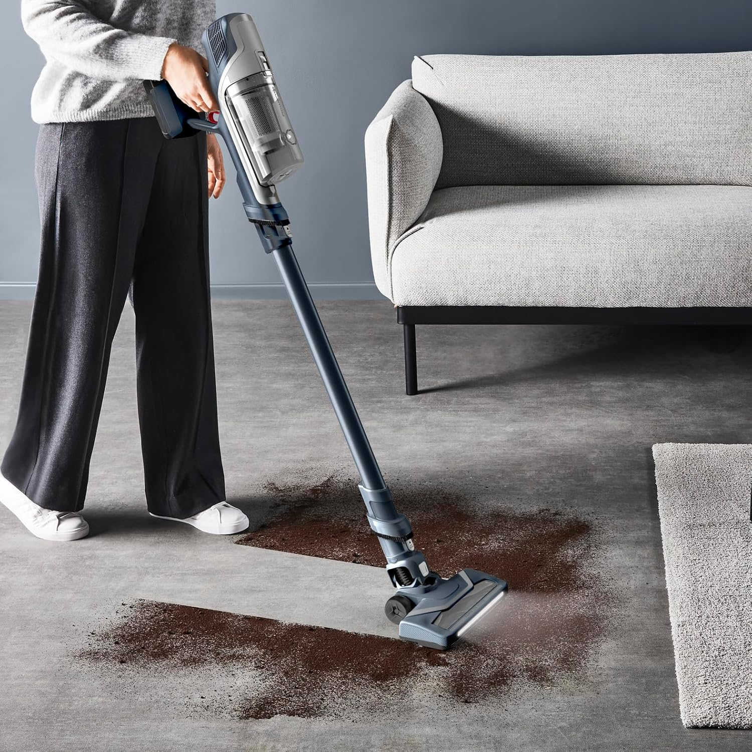 Osoba odkurza brud na betonowej podłodze odkurzaczem bezprzewodowym.