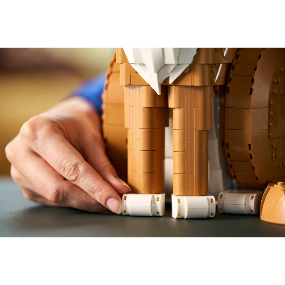 Ręka umieszcza białe klocki Lego pod brązowymi klockami Lego tworzącymi nogi.