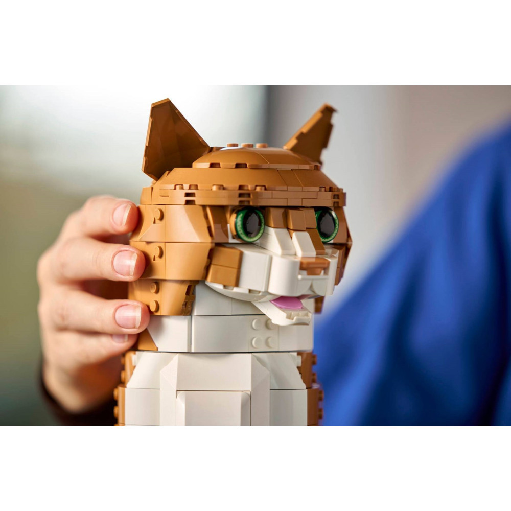 Osoba trzyma brązowo-białego kota z Lego, z zielonymi oczami i różowym językiem.