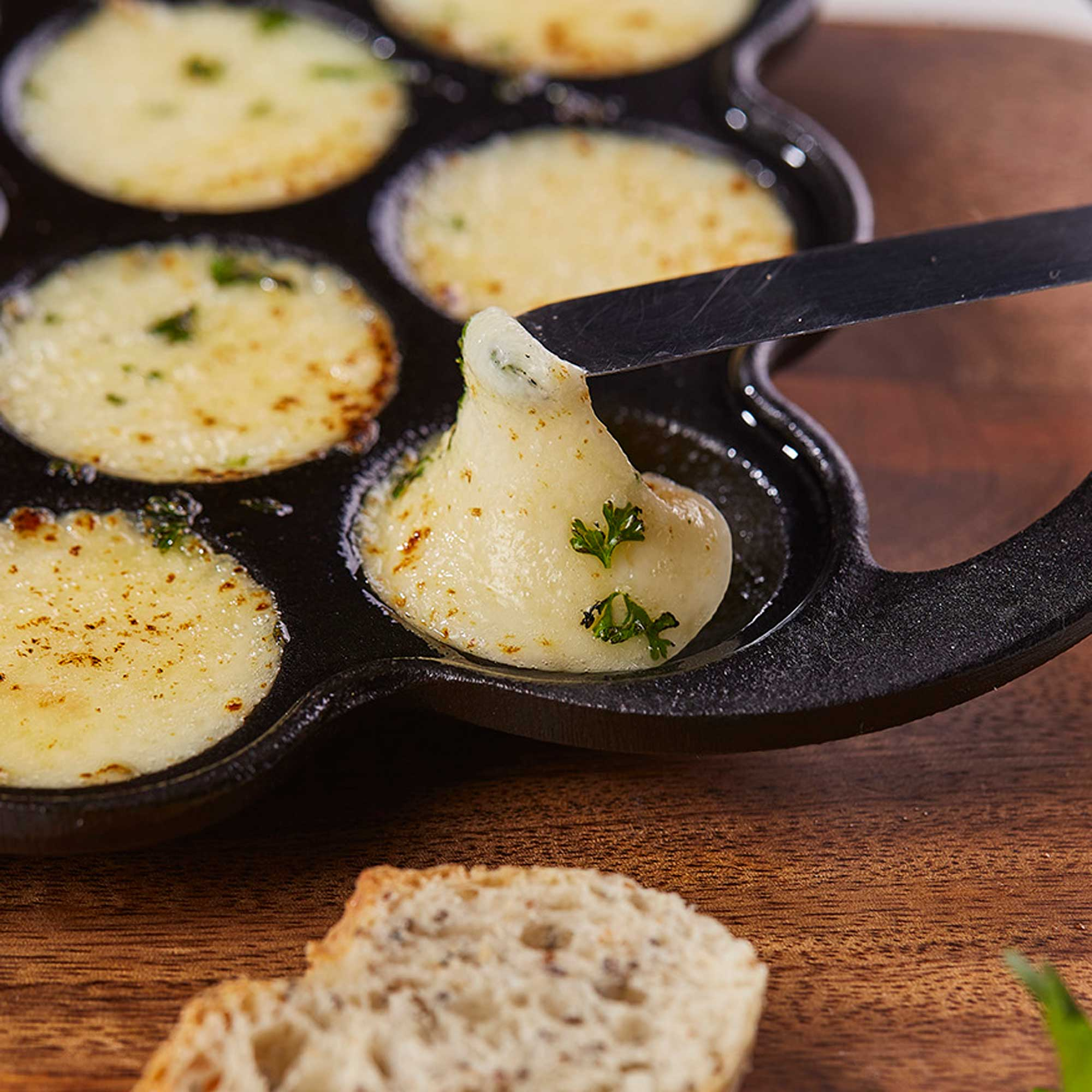 Queso derretido con hierbas en una sartén, al lado pan.