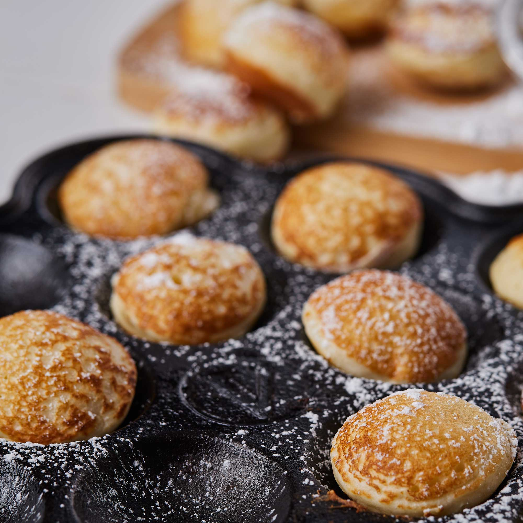 Mini panqueques espolvoreados con azúcar glas en sartén de hierro.