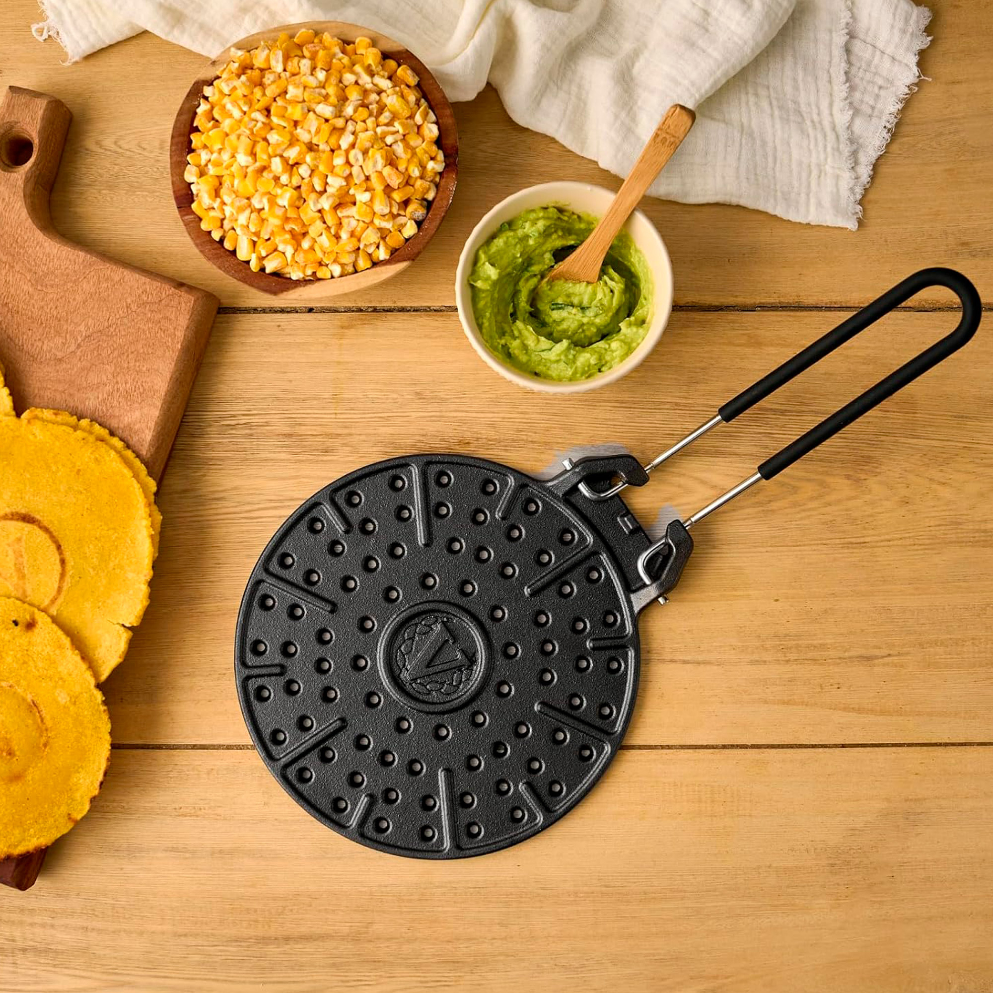 Ein schwarzes Grillgerät mit Griffen, daneben Mais, Avocado und Tortillas.