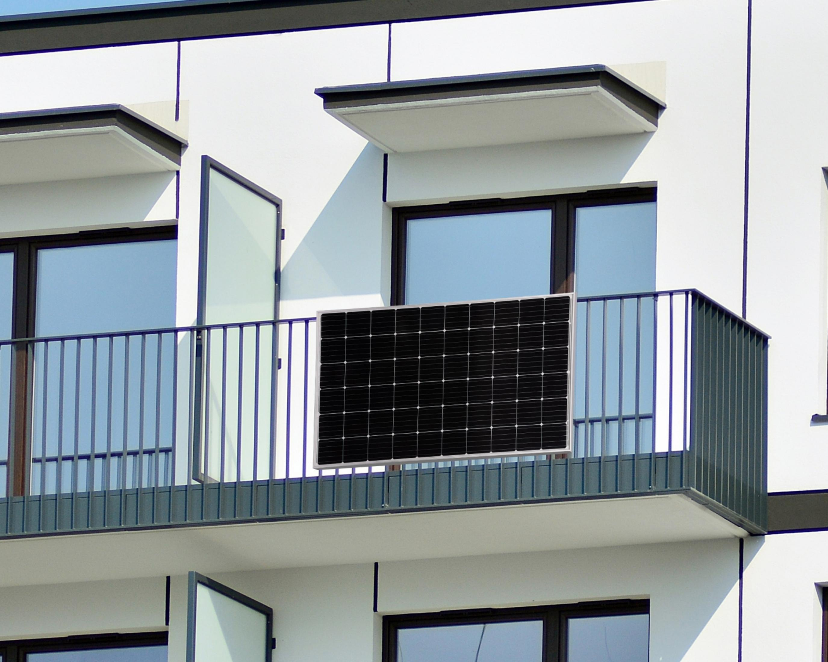 Un pannello solare nero poggia sulla ringhiera di un balcone di fronte a un edificio bianco.