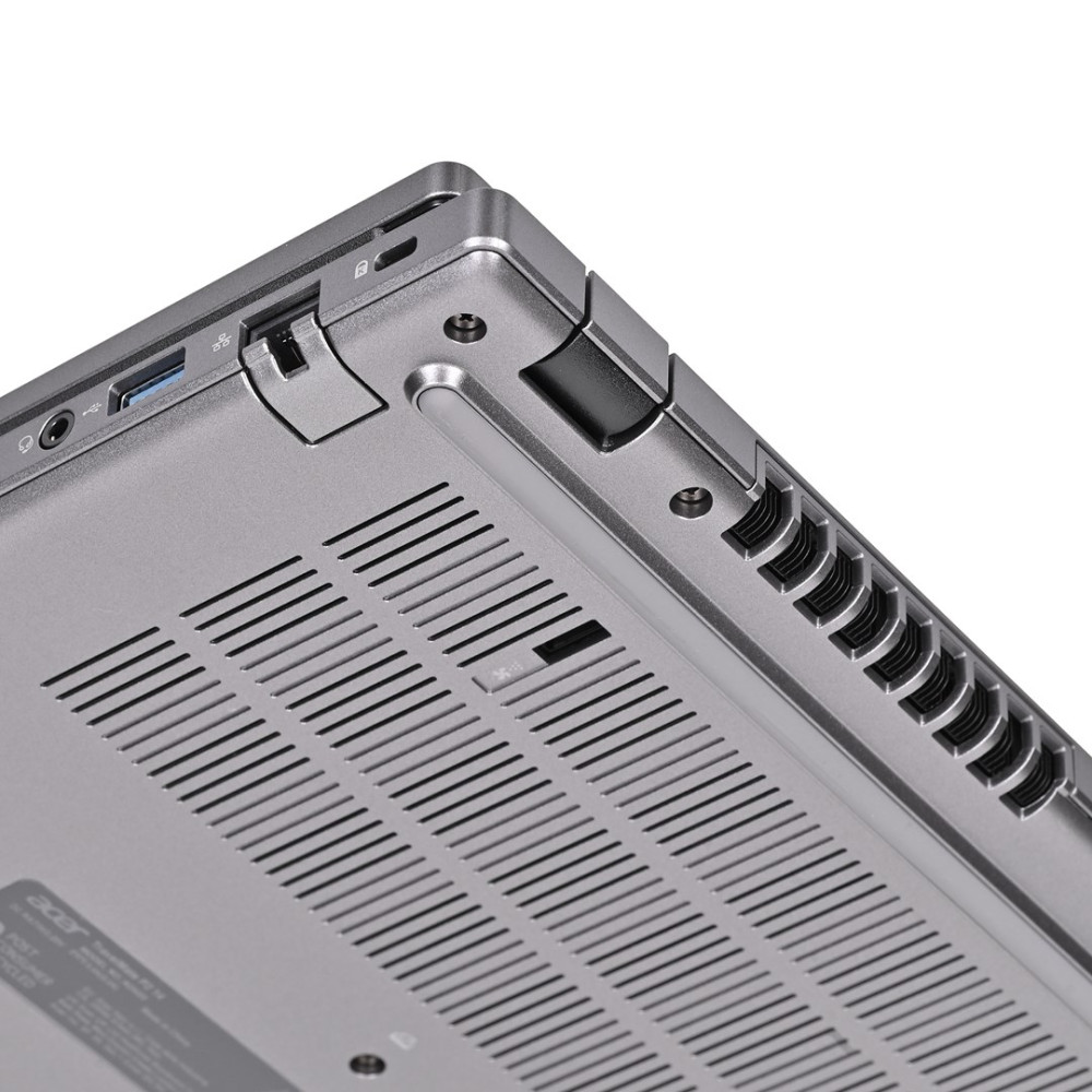 Zbliżenie dolnej krawędzi srebrnego laptopa, pokazujące otwory wentylacyjne, porty USB i gniazdo audio.