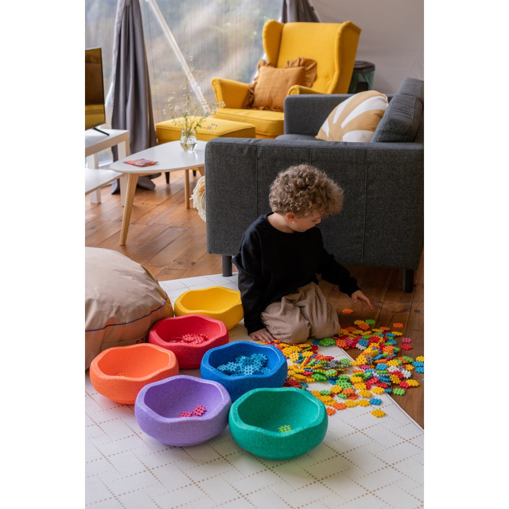 Un niño juega con bloques de construcción coloridos en cuencos en el suelo.