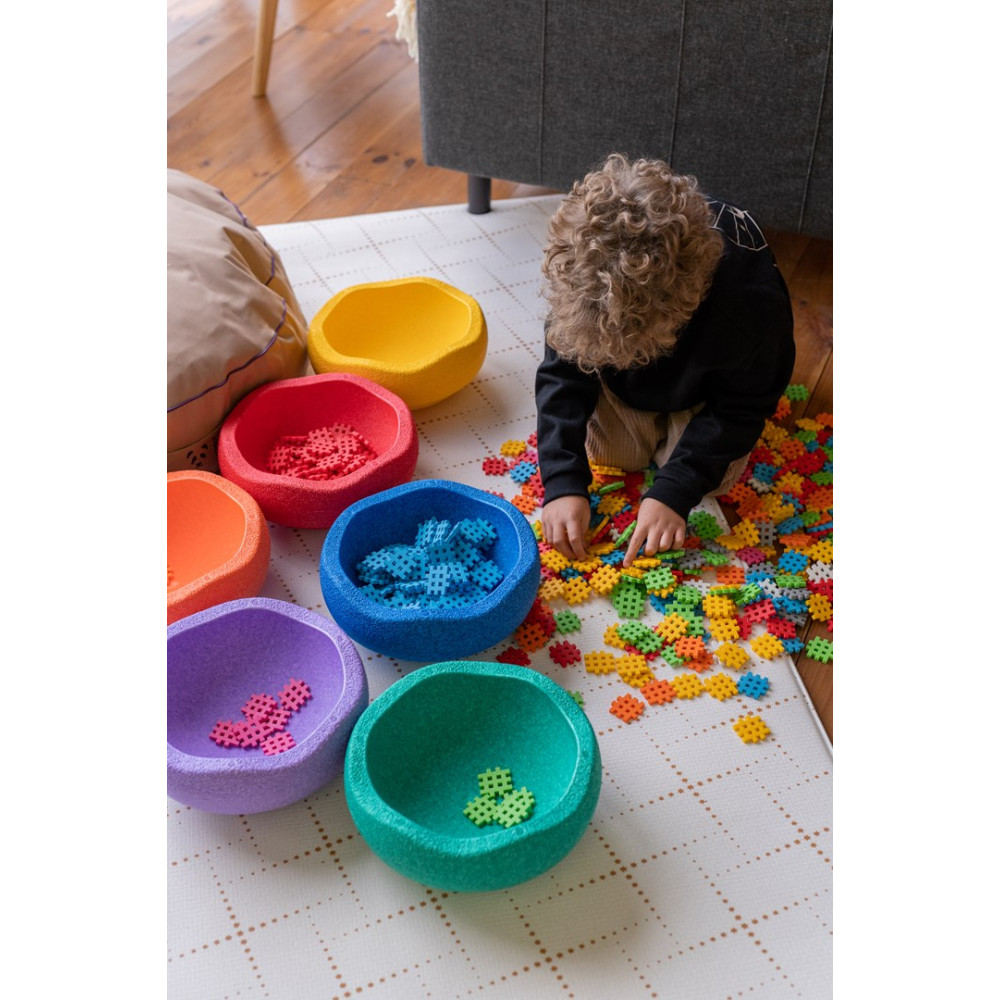 Un niño juega con bloques de construcción coloridos en cuencos sobre una alfombra.