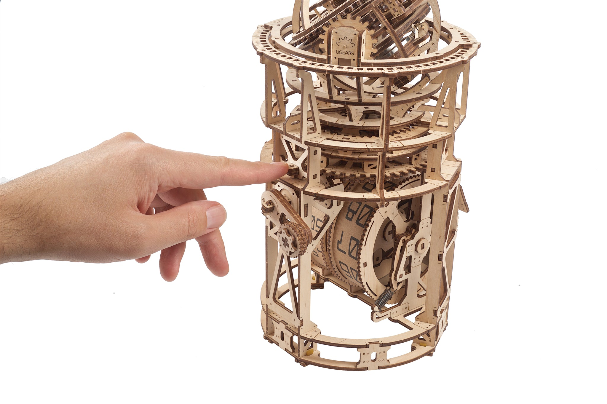 Ein Finger tippt auf ein detailliertes Holzmodell mit Zahnrädern und Zifferblättern.