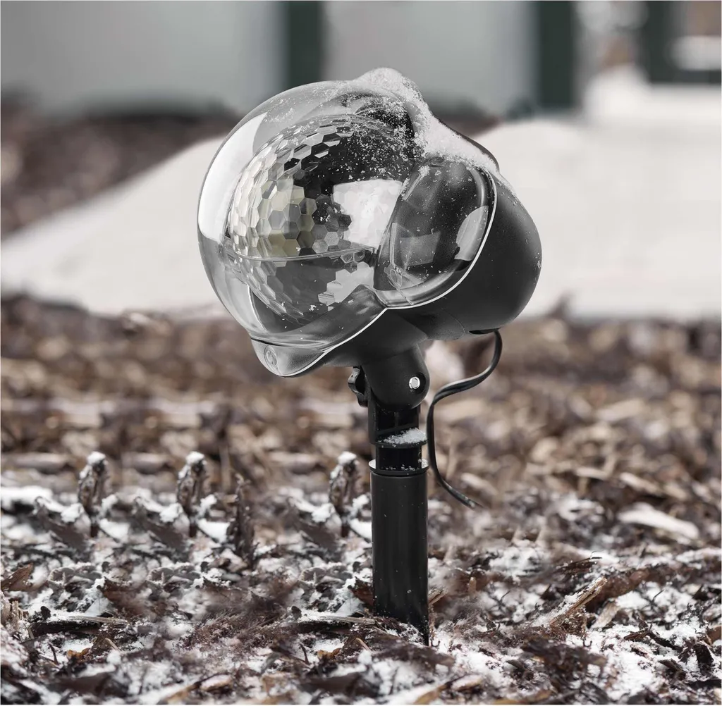 Schneebedeckter Lichterprojektor im Freien auf einem Untergrund aus Rindenmulch.
