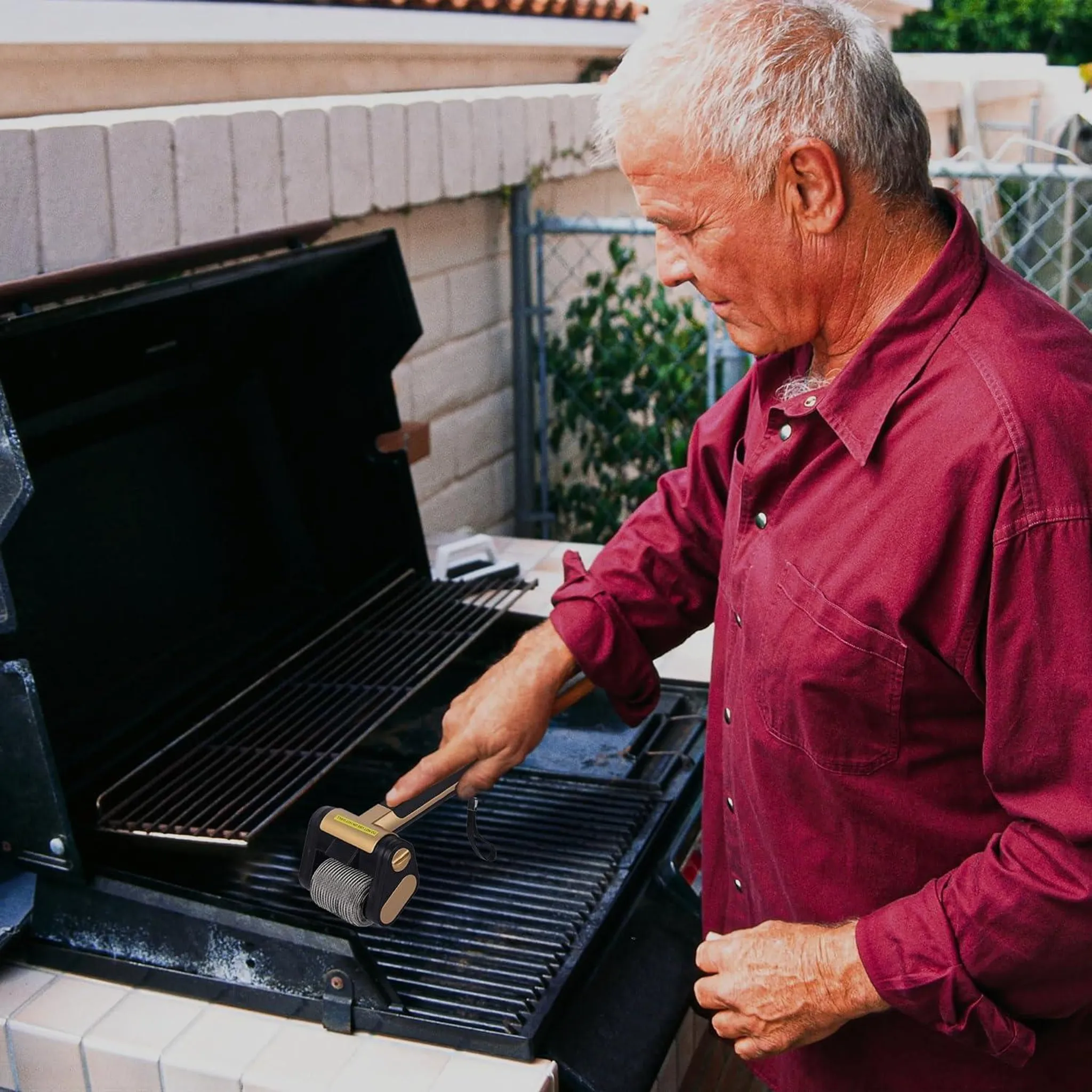 Ein älterer Mann in einem roten Hemd reinigt einen Grill mit einem Werkzeug.