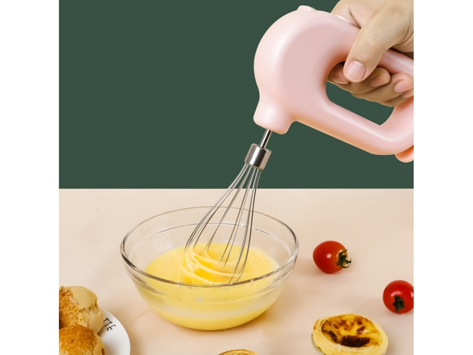 Ein rosa Handmixer schlägt Eier in einer Glasschüssel, daneben Gebäck und Tomaten.