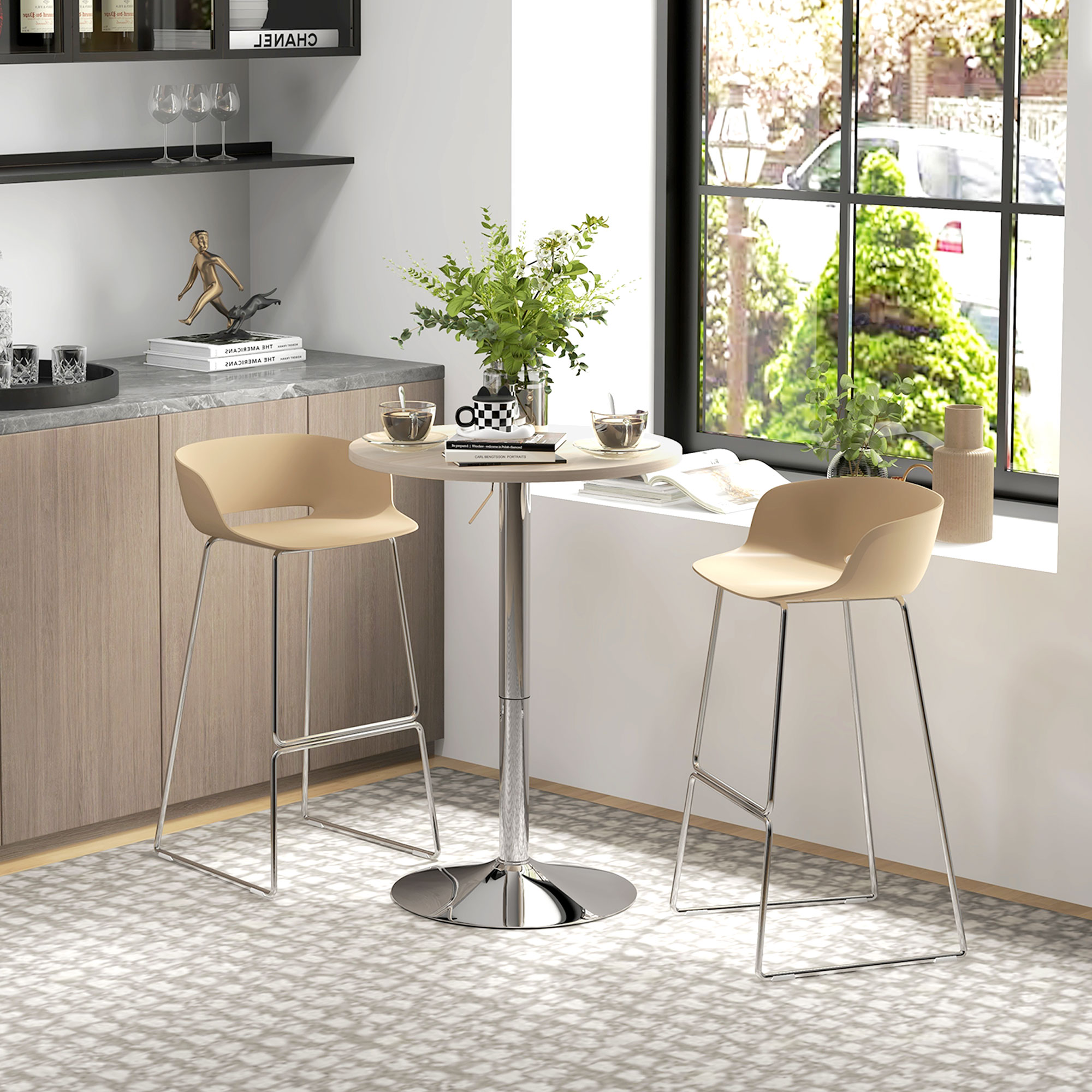 Una mesa redonda con dos taburetes altos beige frente a una ventana con vistas a árboles.