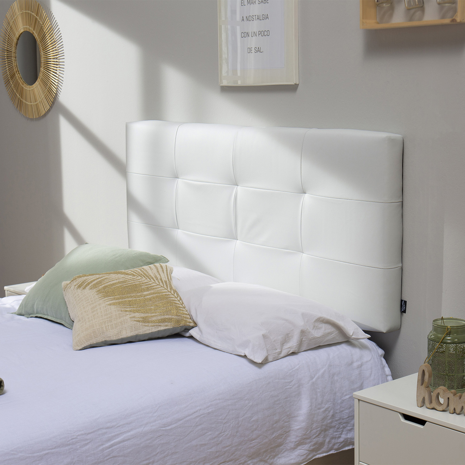 Un cabecero blanco capitoné con tres cojines sobre una cama con sábanas blancas.