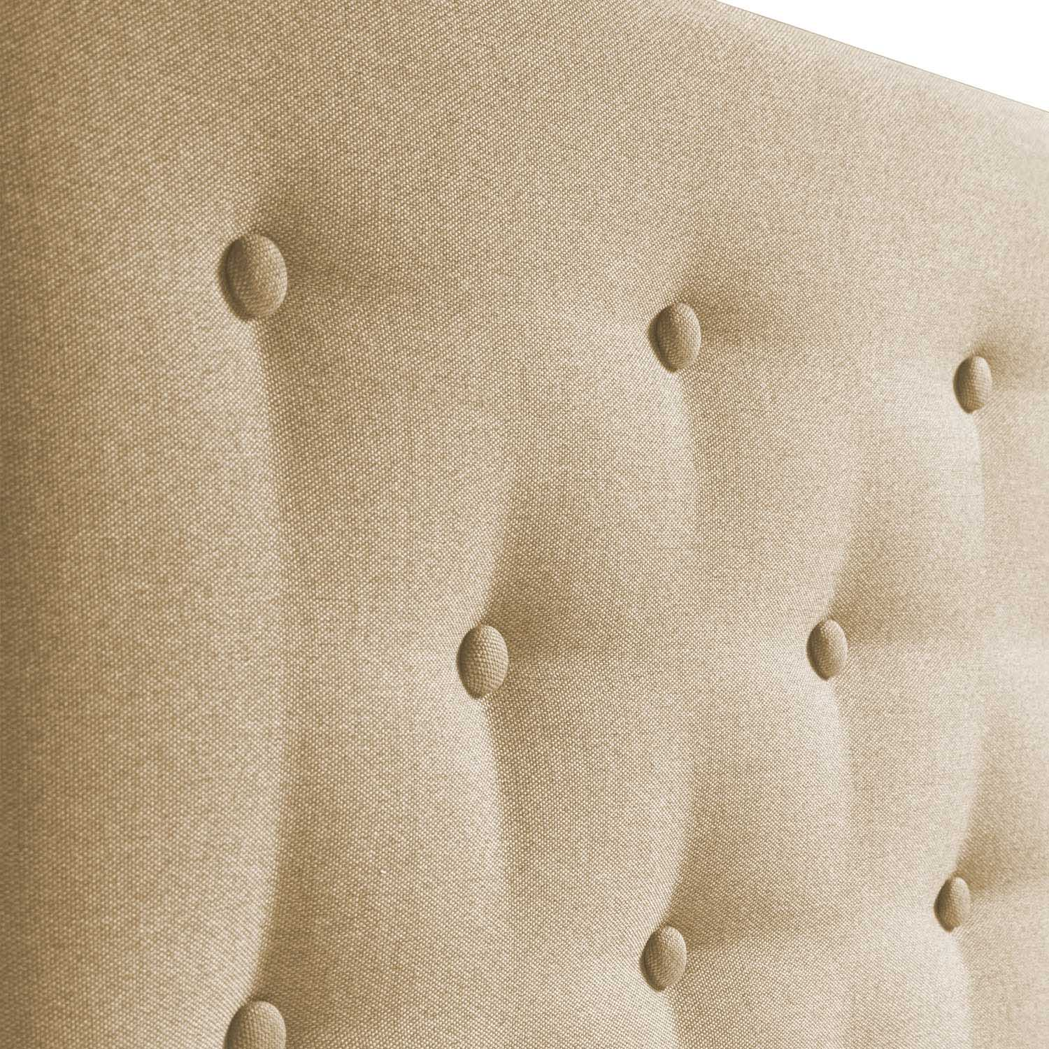 Primer plano de un cabecero de tela beige con botones capitoné.