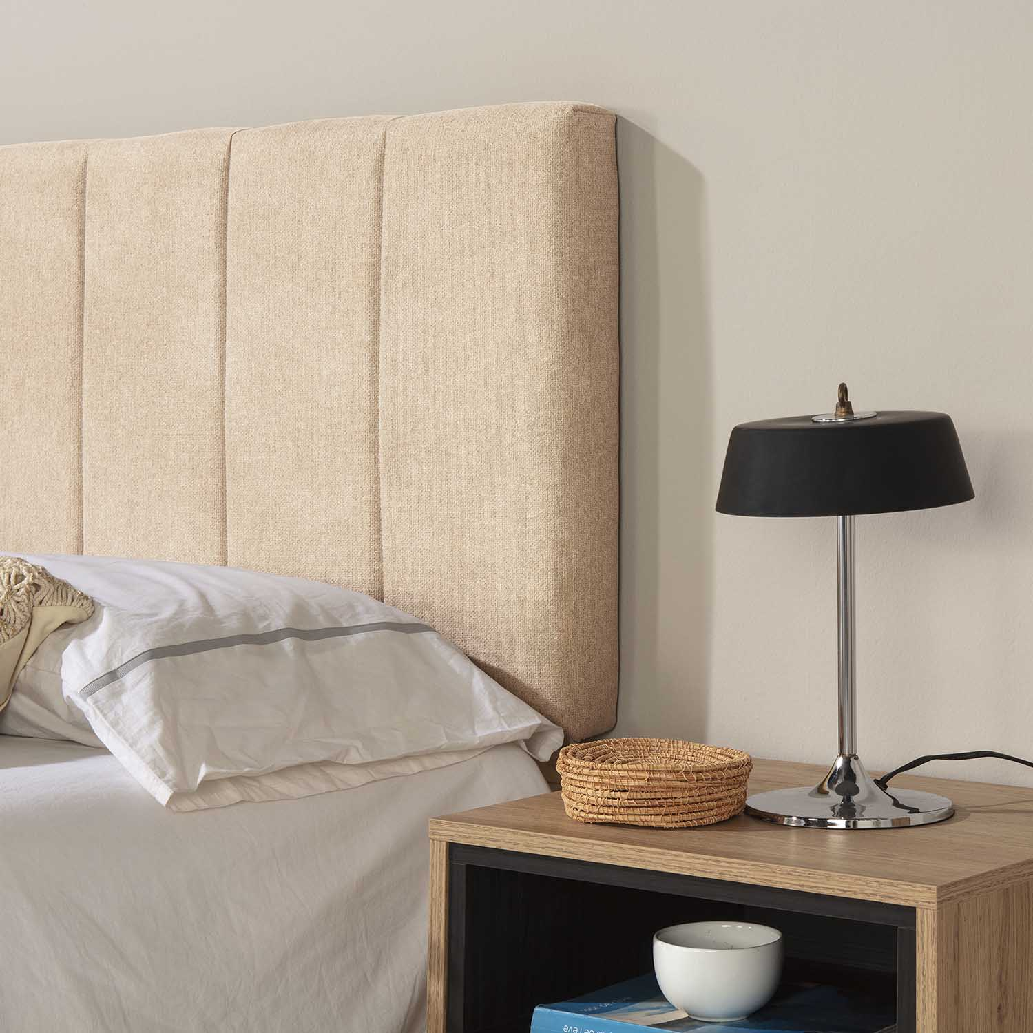 Un cabecero beige, mesita de noche con lámpara, cesta y cuenco.
