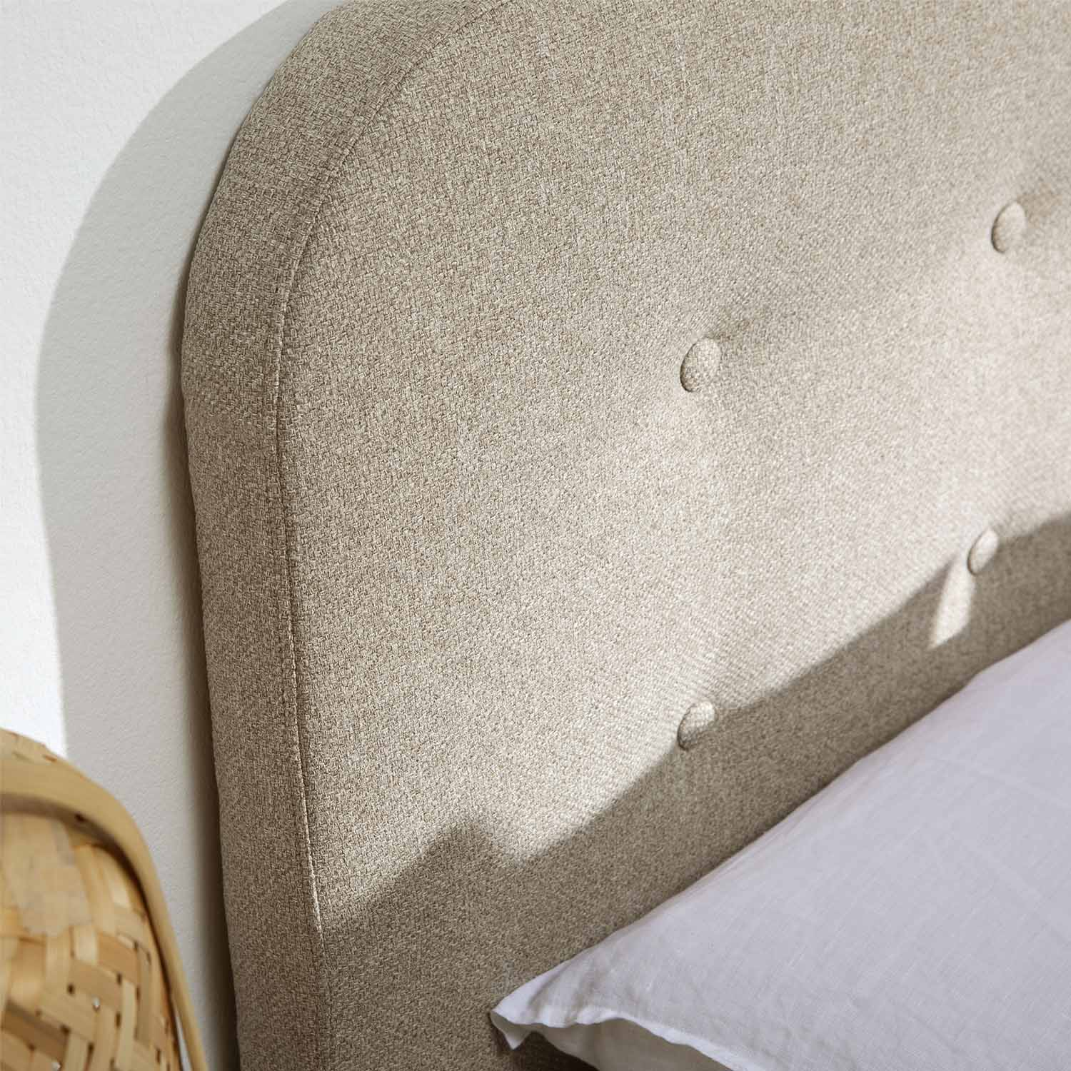 Cabecero tapizado beige con botones y una almohada blanca al lado.