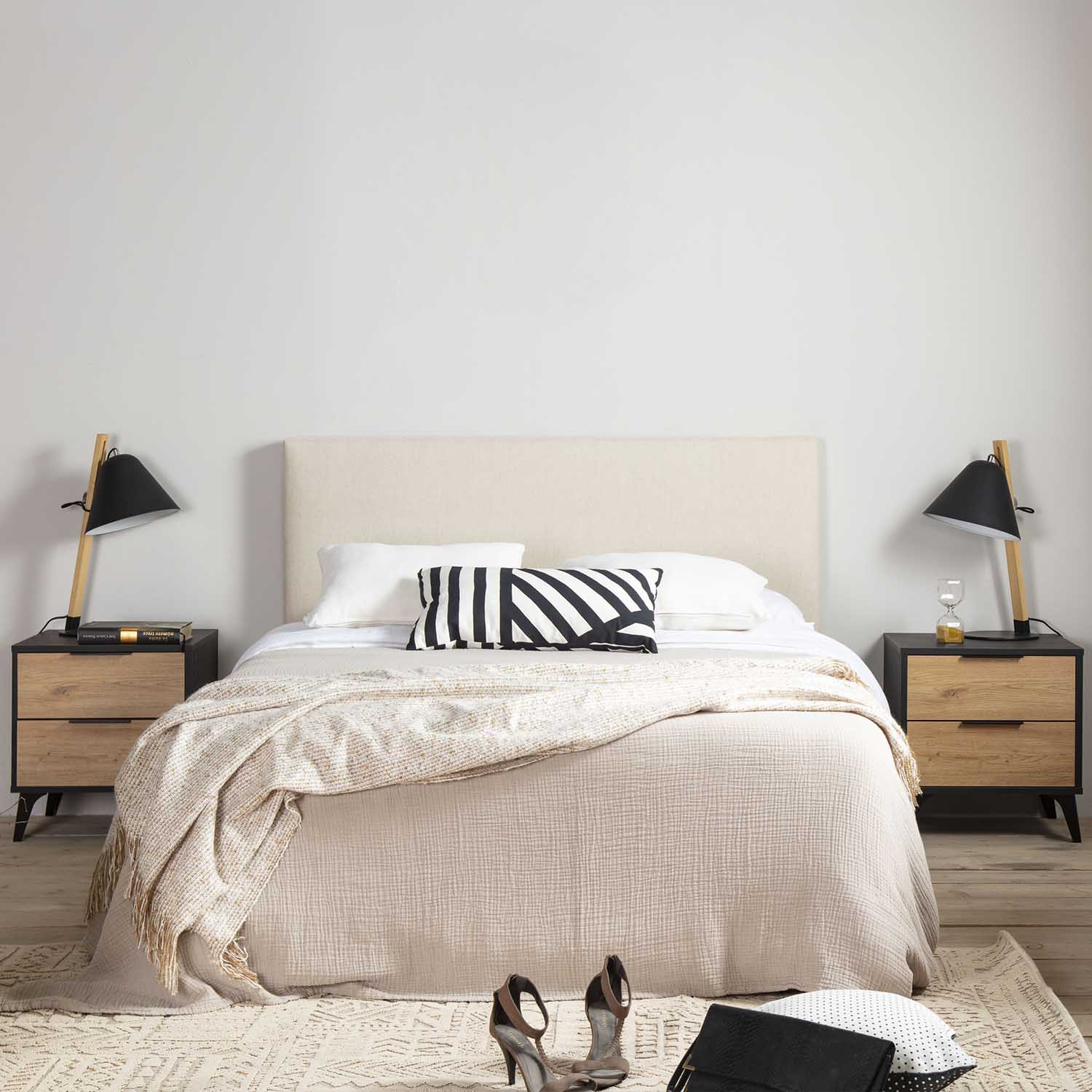 Un dormitorio moderno con cabecero beige, dos mesitas de noche, lámparas y una cama con mantas.