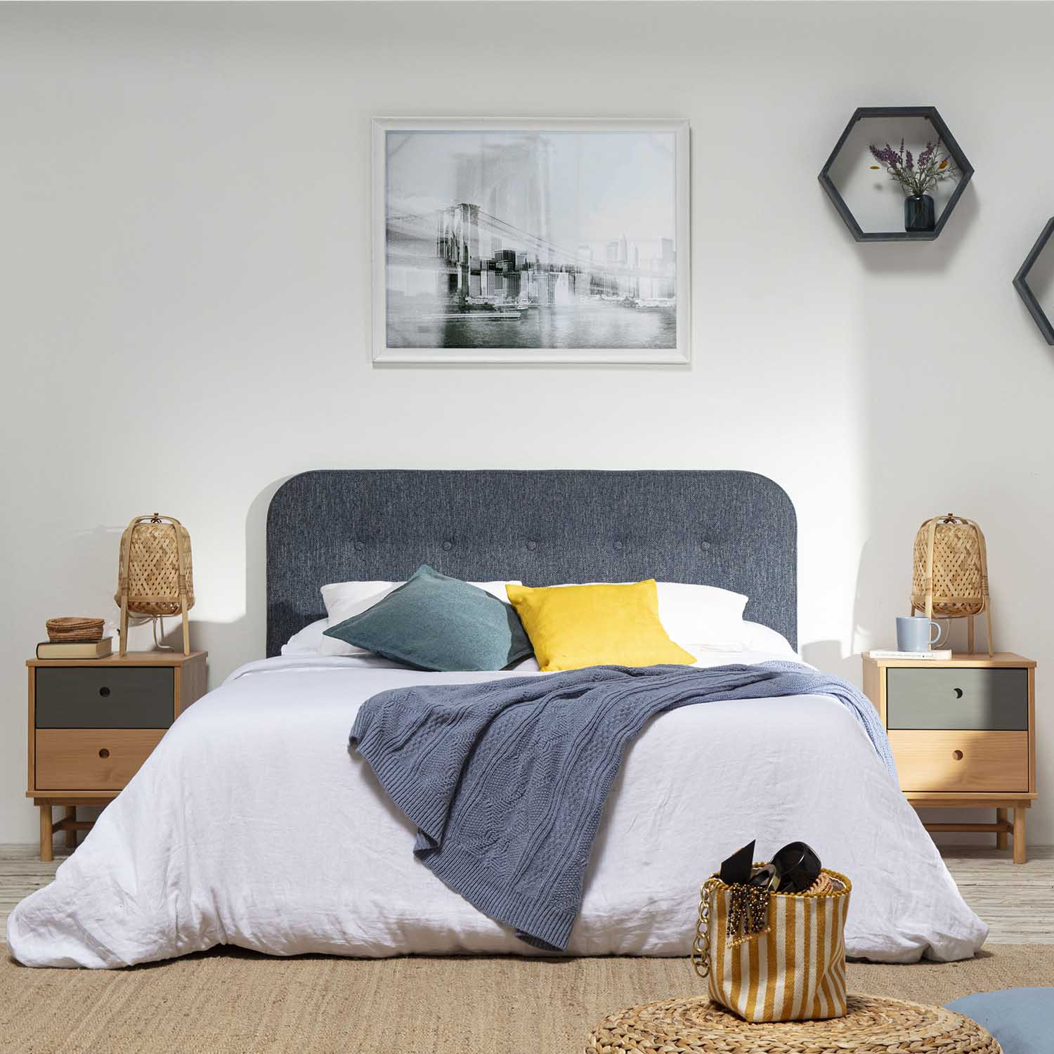 Un dormitorio con cama blanca, cojines azules y amarillos, manta y mesitas de noche.