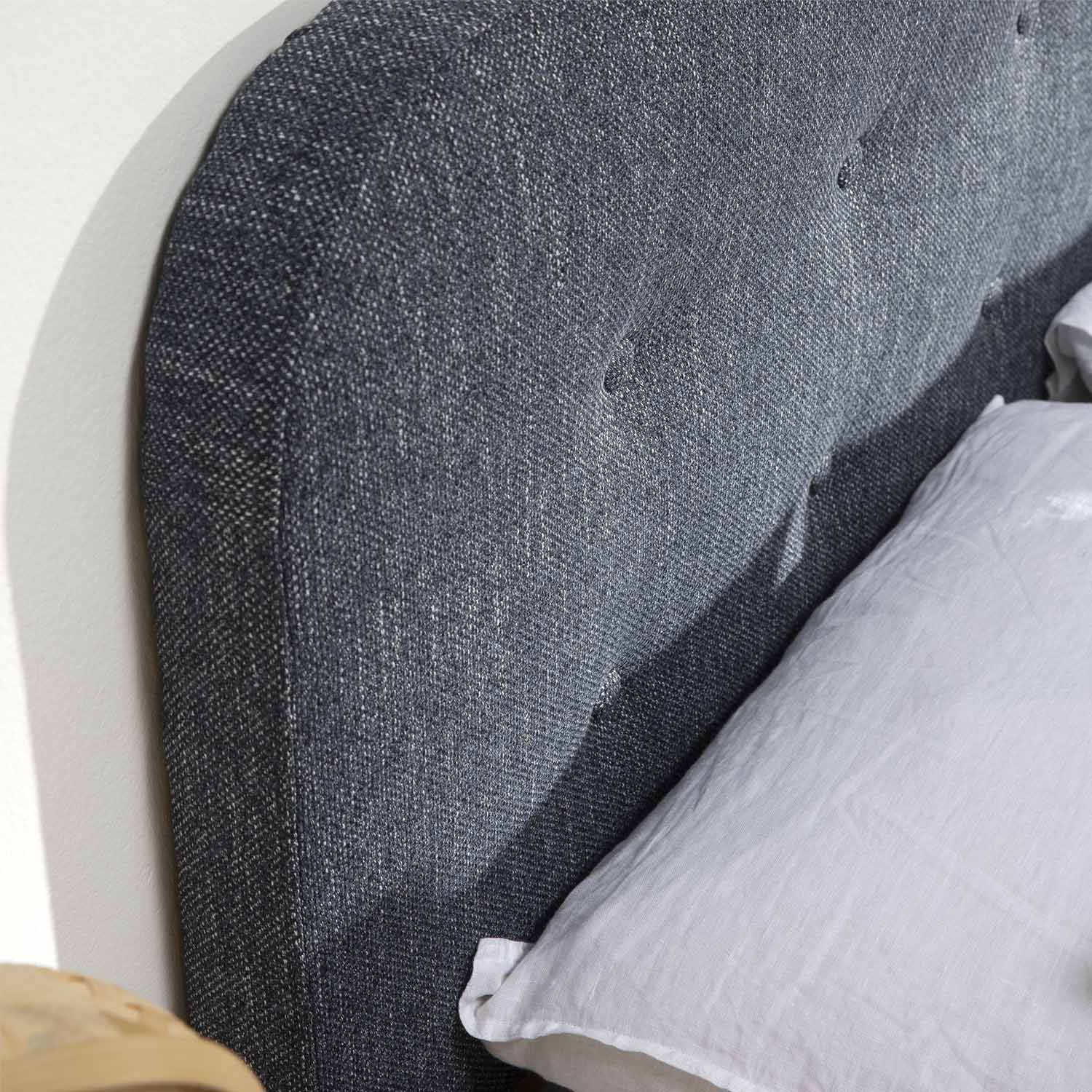Un cabecero gris oscuro tapizado con una almohada blanca a la derecha.