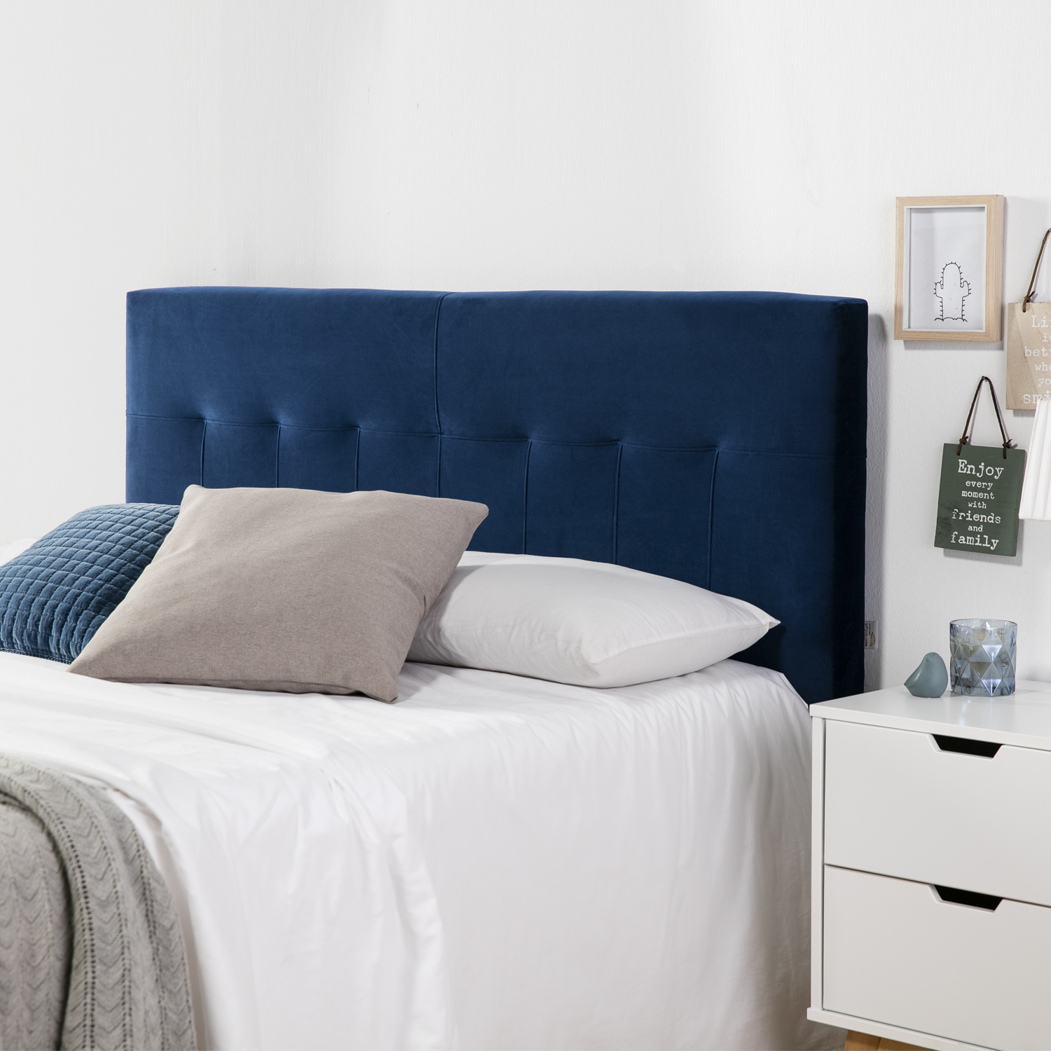 Un cabecero azul sobre una cama con sábanas blancas, almohadas y una manta.