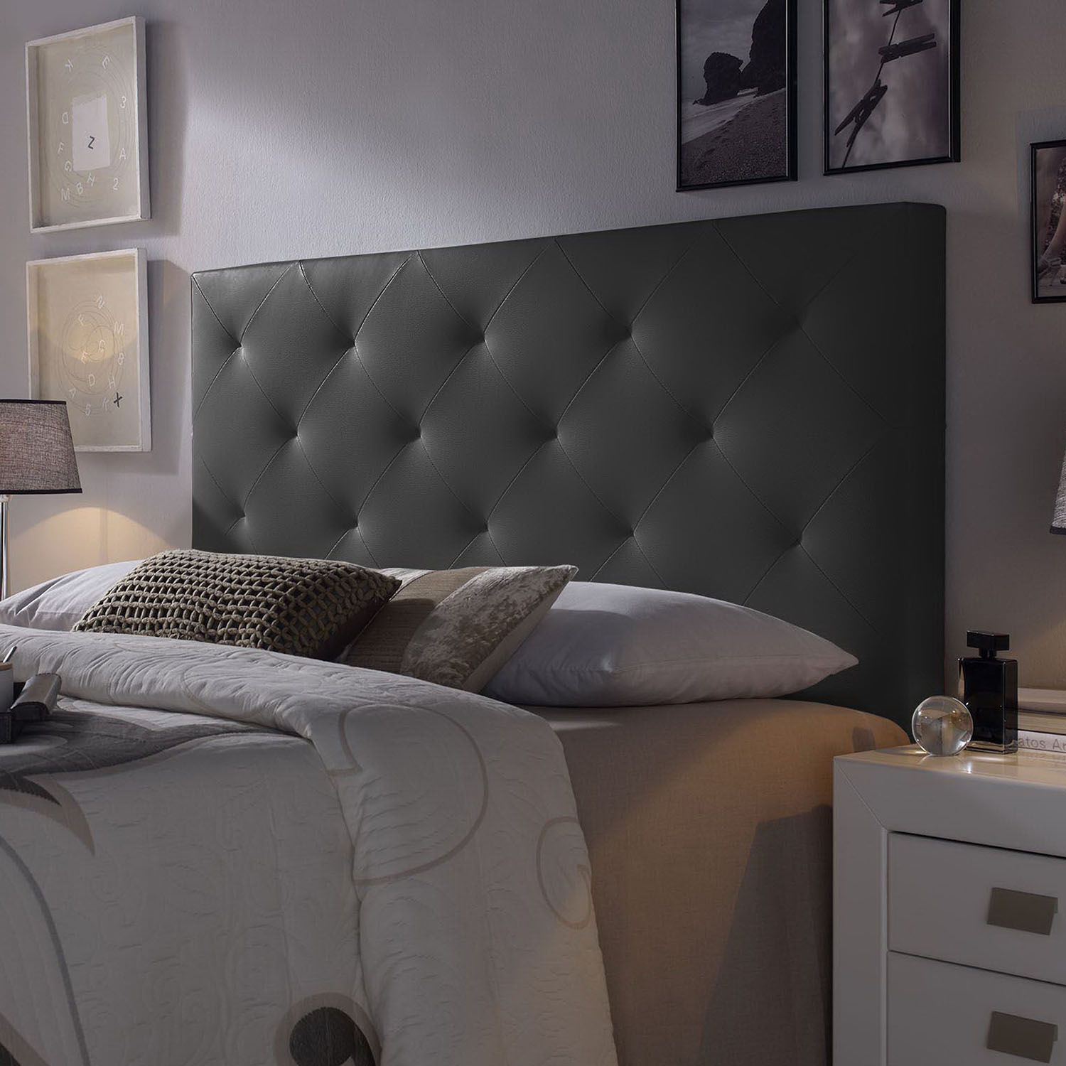 Un cabecero gris capitoné sobre una cama con almohadas y un edredón blanco estampado.