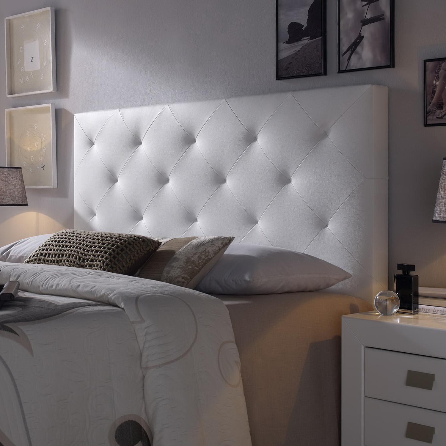 Un cabecero blanco acolchado con almohadas y edredón en una cama.