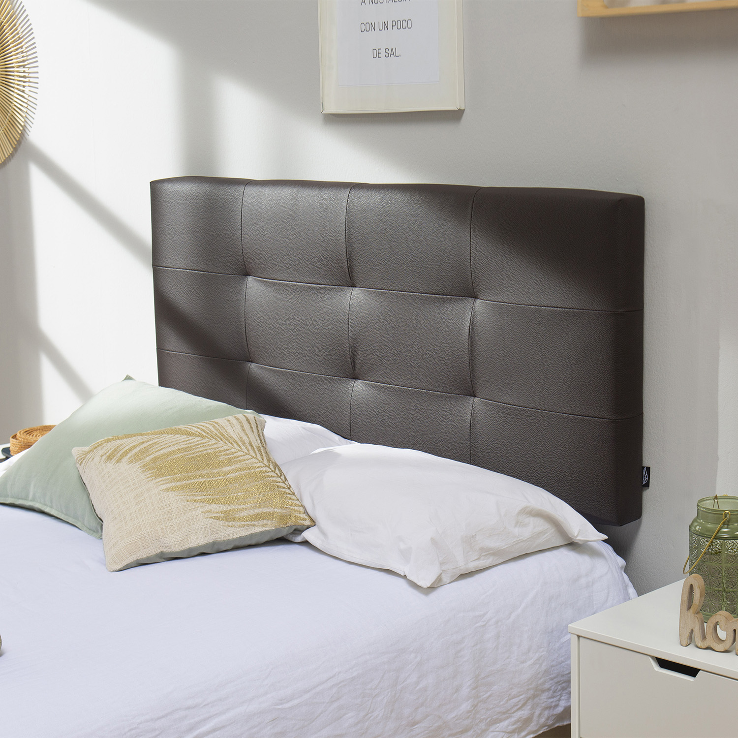 Un cabecero oscuro con botones sobre una cama con sábanas y almohadas blancas.