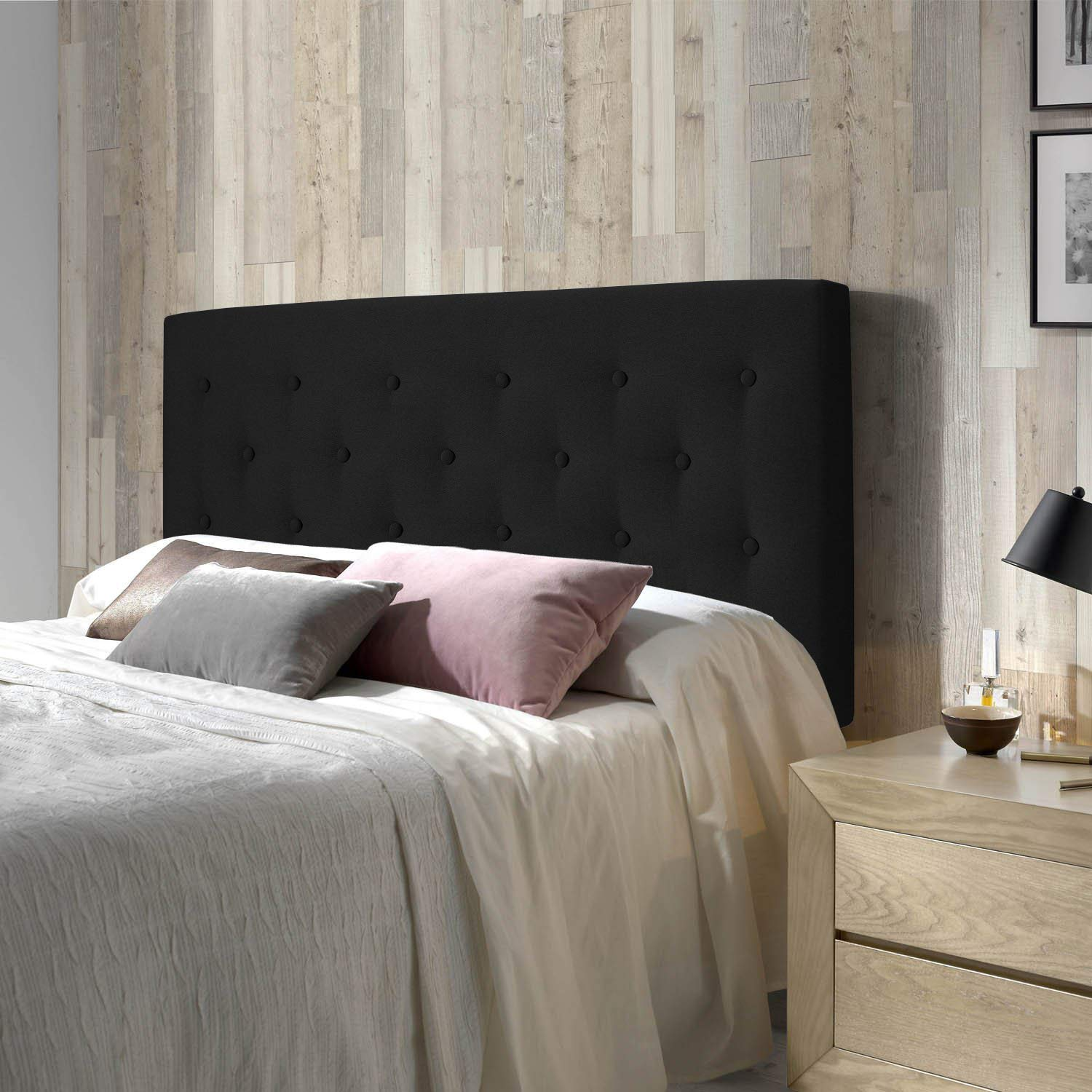 Un cabecero negro capitoné se alza tras una cama con ropa de cama blanca y cojines decorativos.