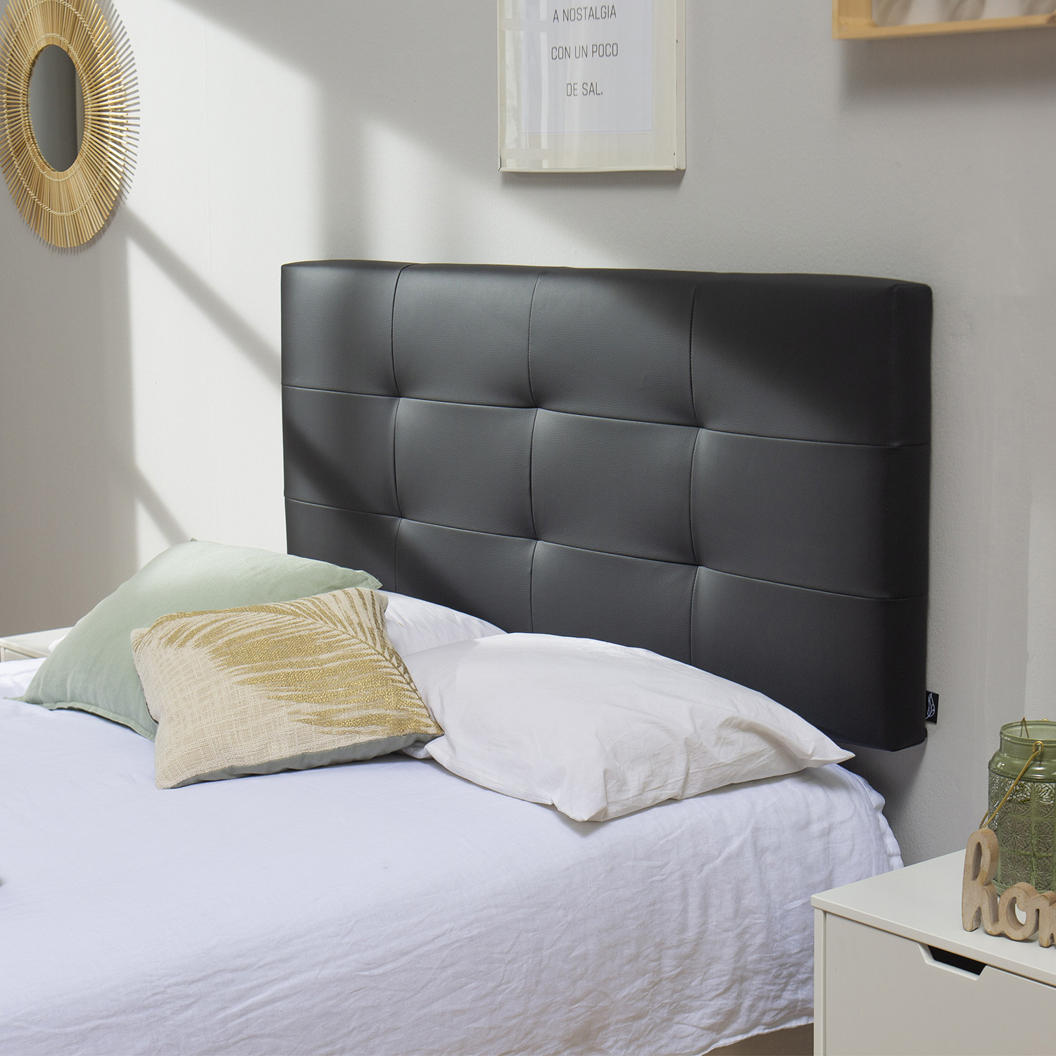 Un cabecero negro capitoné con ropa de cama blanca y cojines decorativos en una cama.