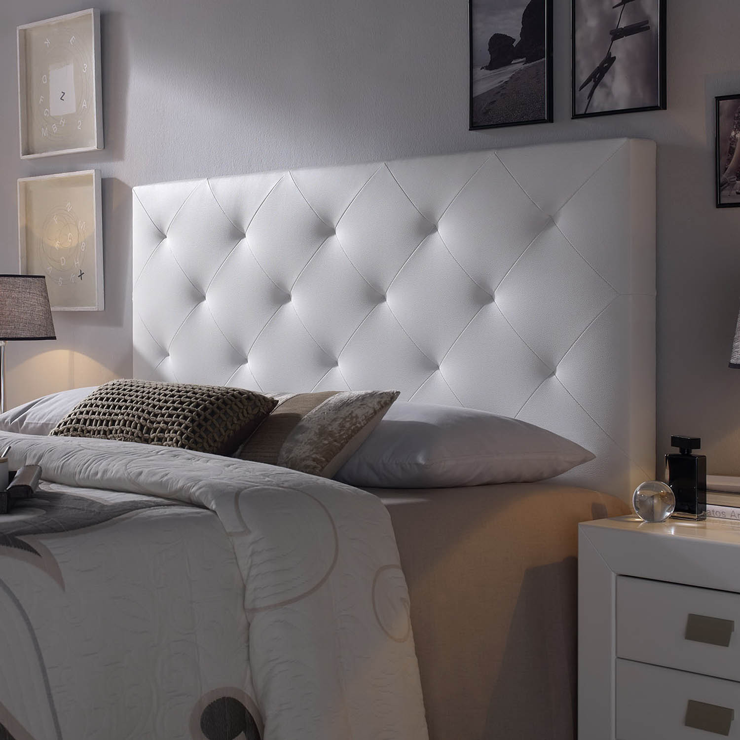 Un cabecero blanco acolchado sobre una cama con almohadas y mantas.