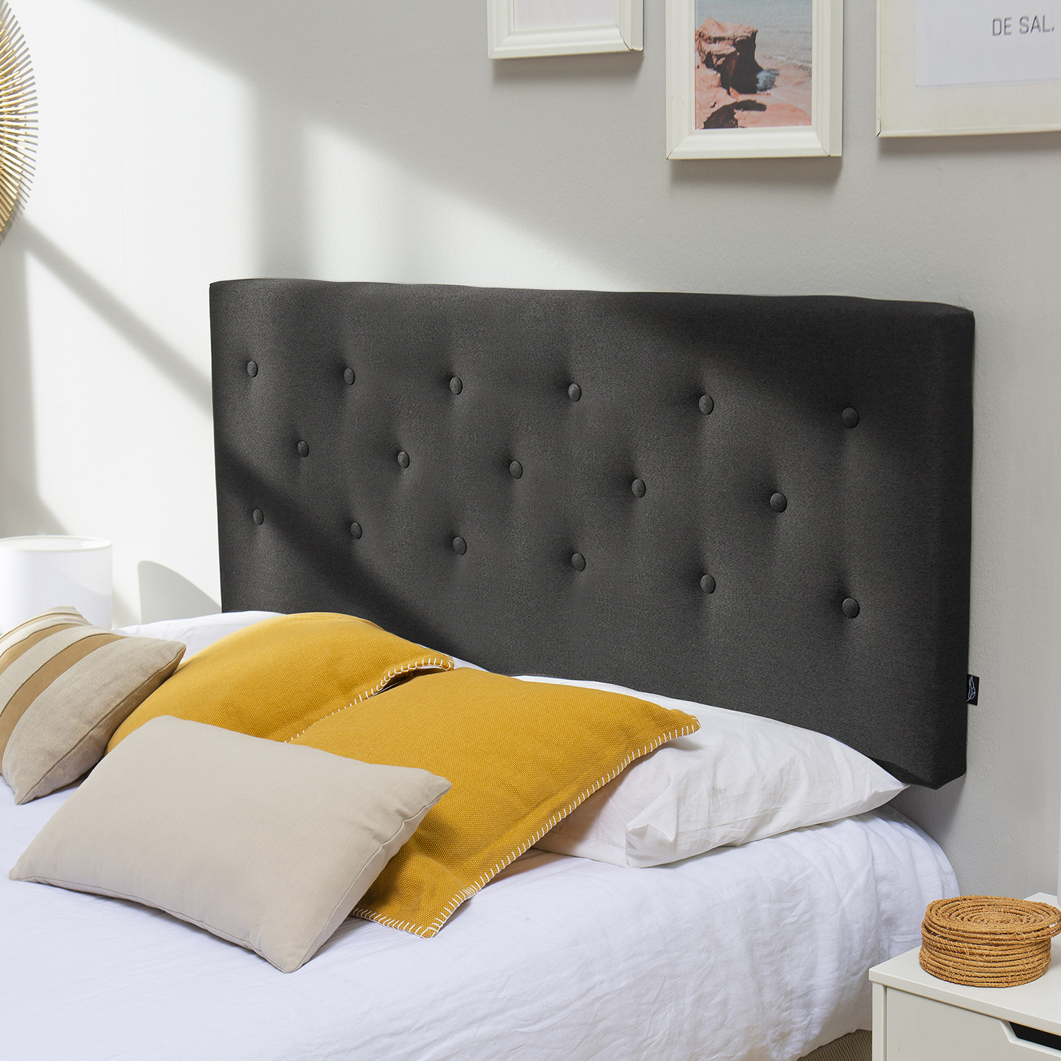 Un cabecero tapizado gris oscuro sobre una cama con almohadas amarillas y beige.