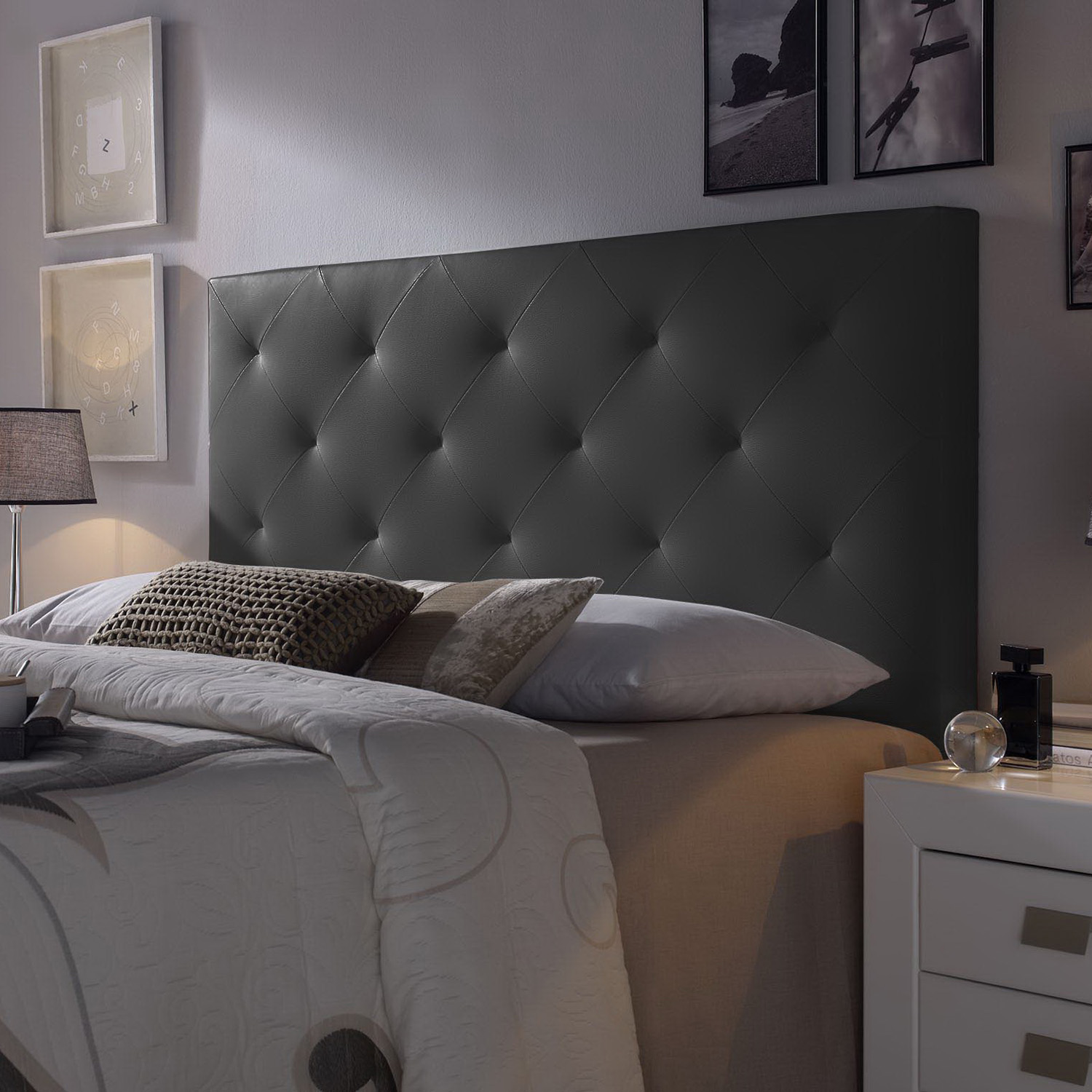 Un cabecero oscuro y tapizado sobre una cama con cojines y mantas.
