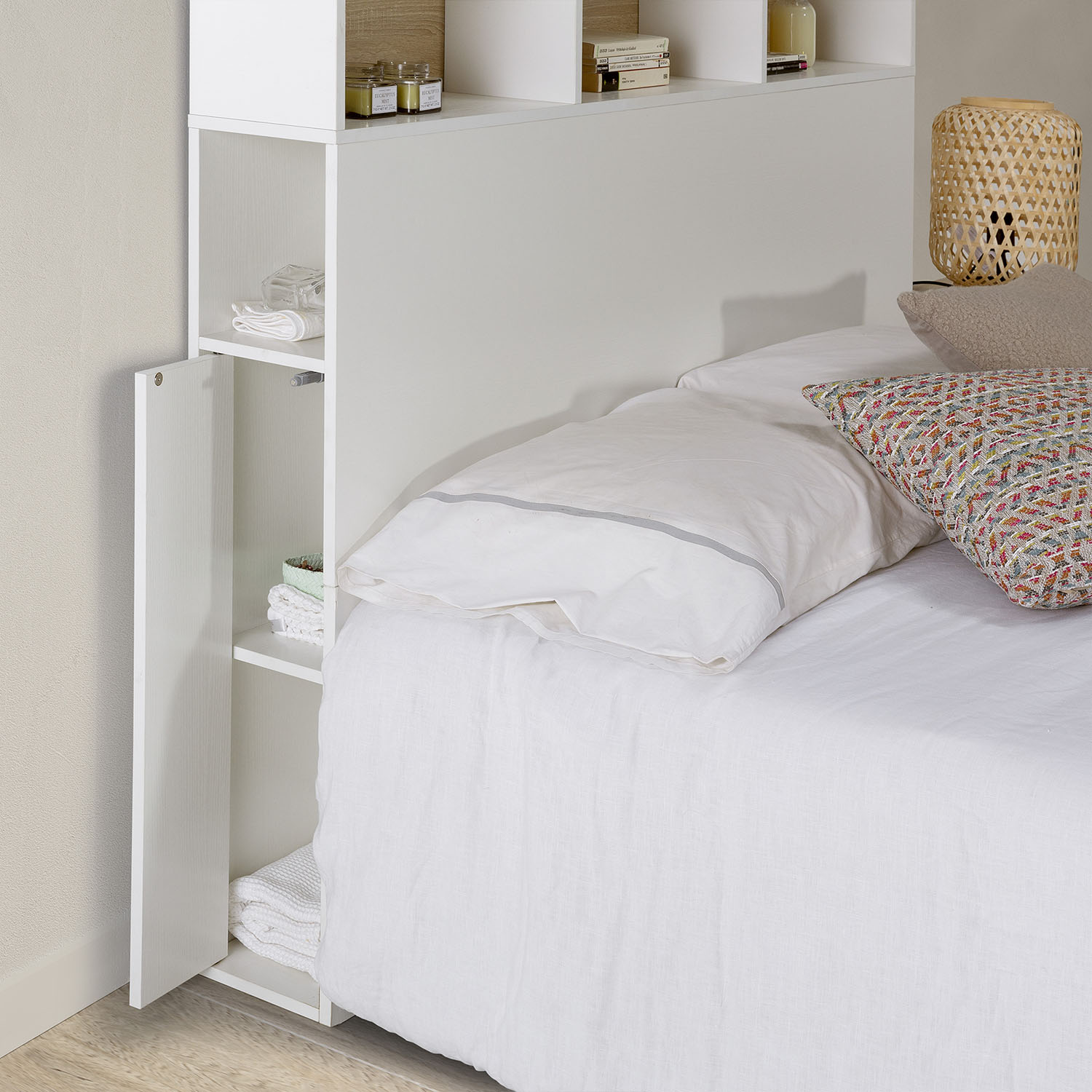 Cama blanca con sábanas y almohadas de lino, junto a un mueble blanco con estantes.