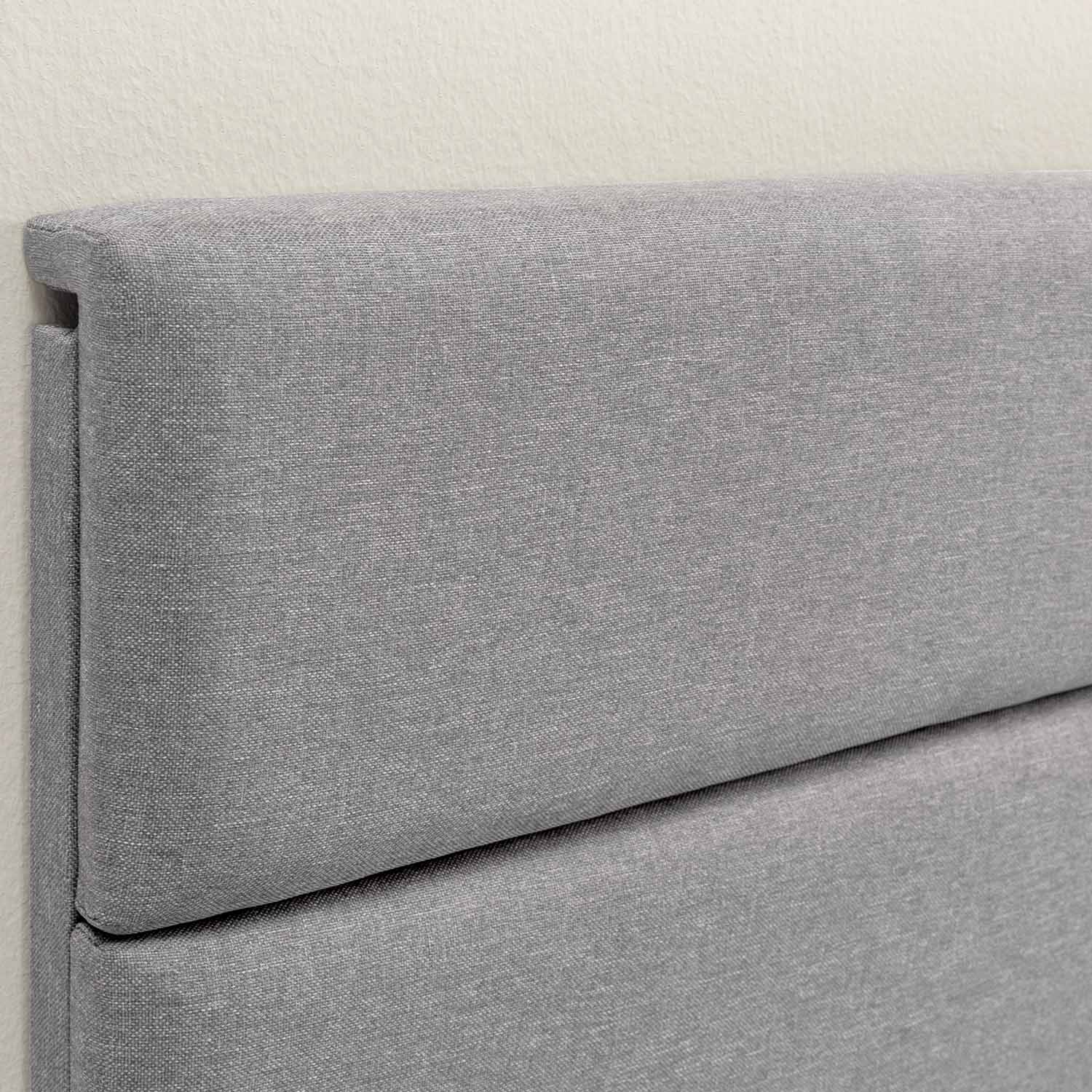 Respaldo de cama de tela gris contra una pared color crema.