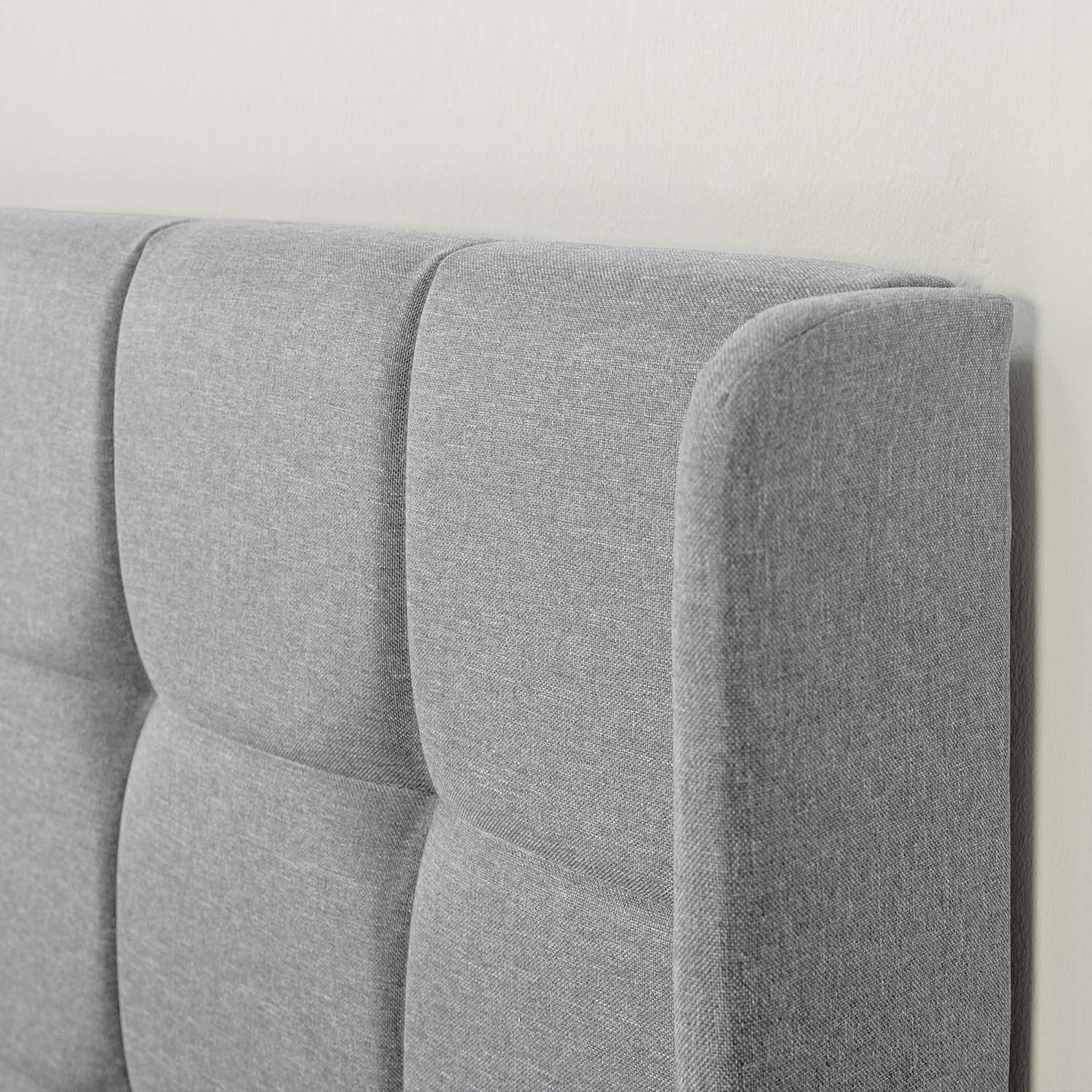 Cabecero de tela gris con capitoné vertical, contra una pared blanca.