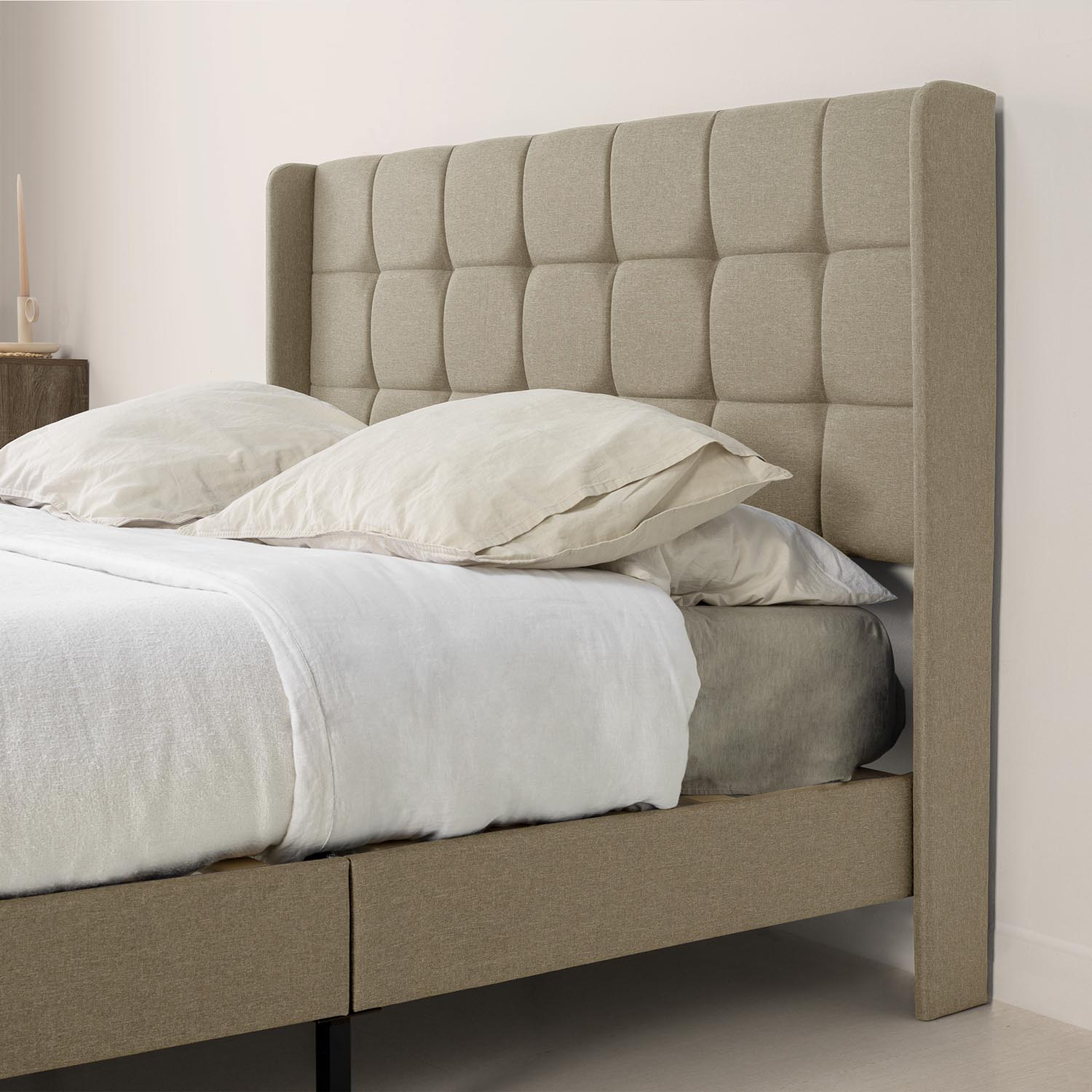Una cama de tela beige con cabecero tapizado y cojines.